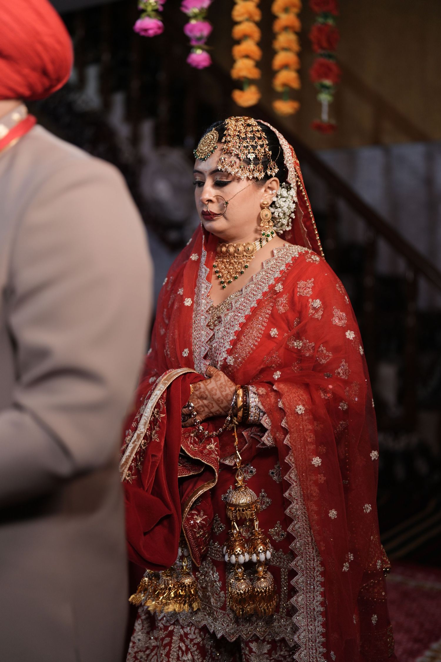 Sikh bride in red bridal lehenga with gold jewelry and kalire during wedding ceremony.