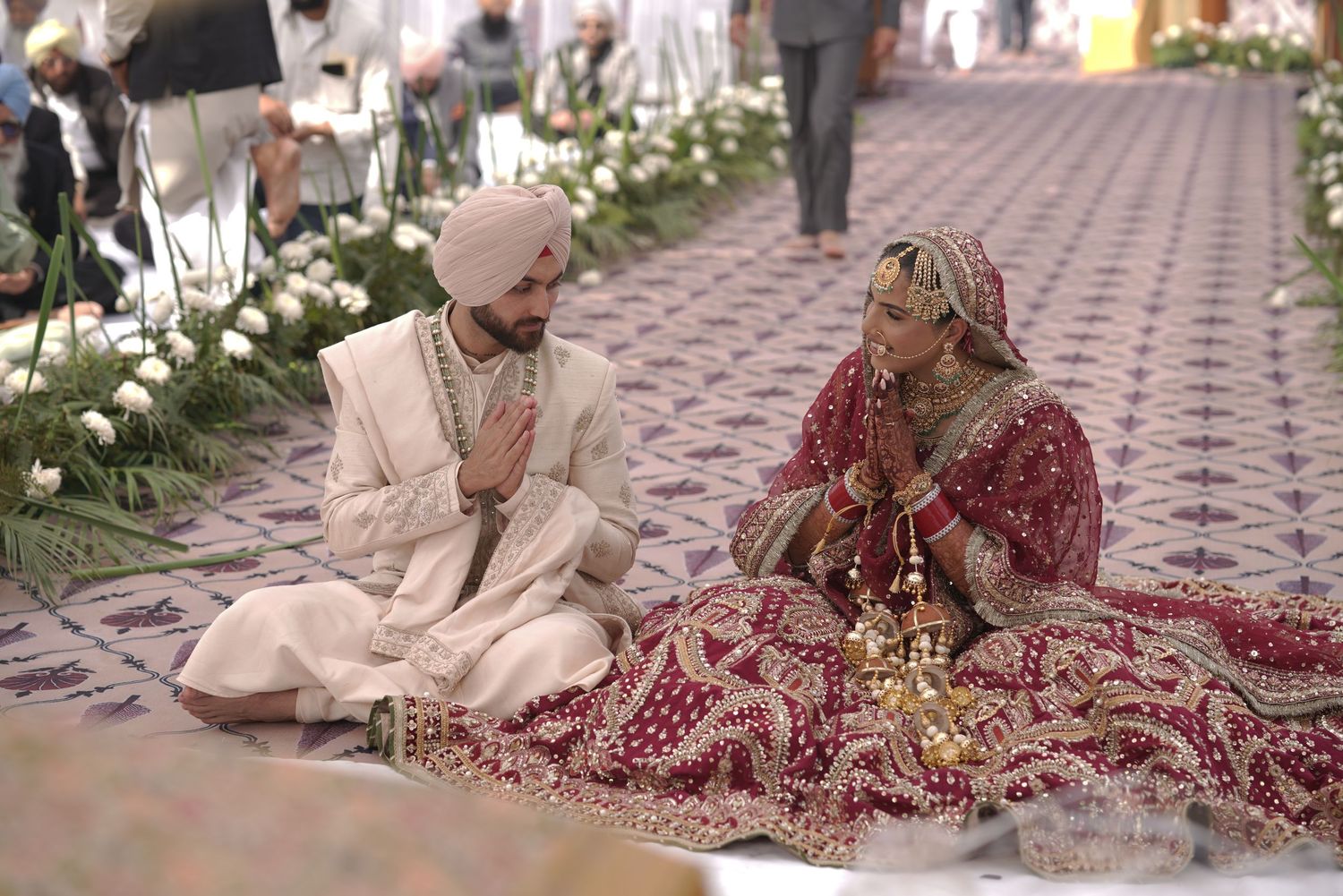 Sikh bride and groom seated during traditional Anand Karaj wedding ceremony with floral decorations.