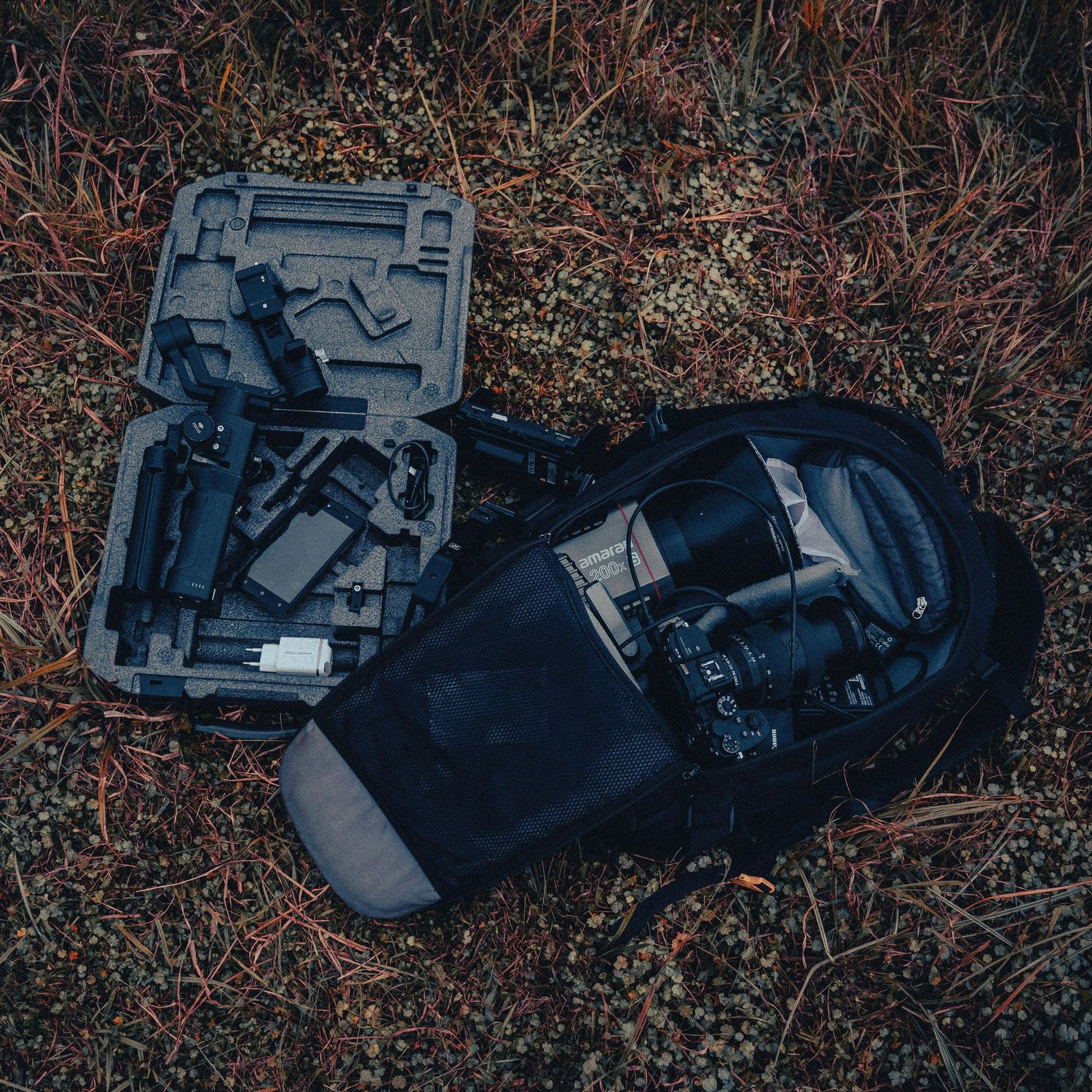 A camera backpack and gimbal stabilizer case laid out on dark forest ground.