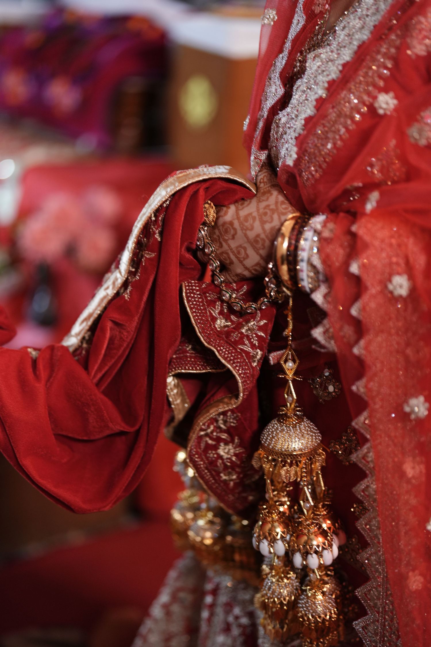 Indian bride in red lehenga holding gold tassel kalire with mehndi hands and bangles.