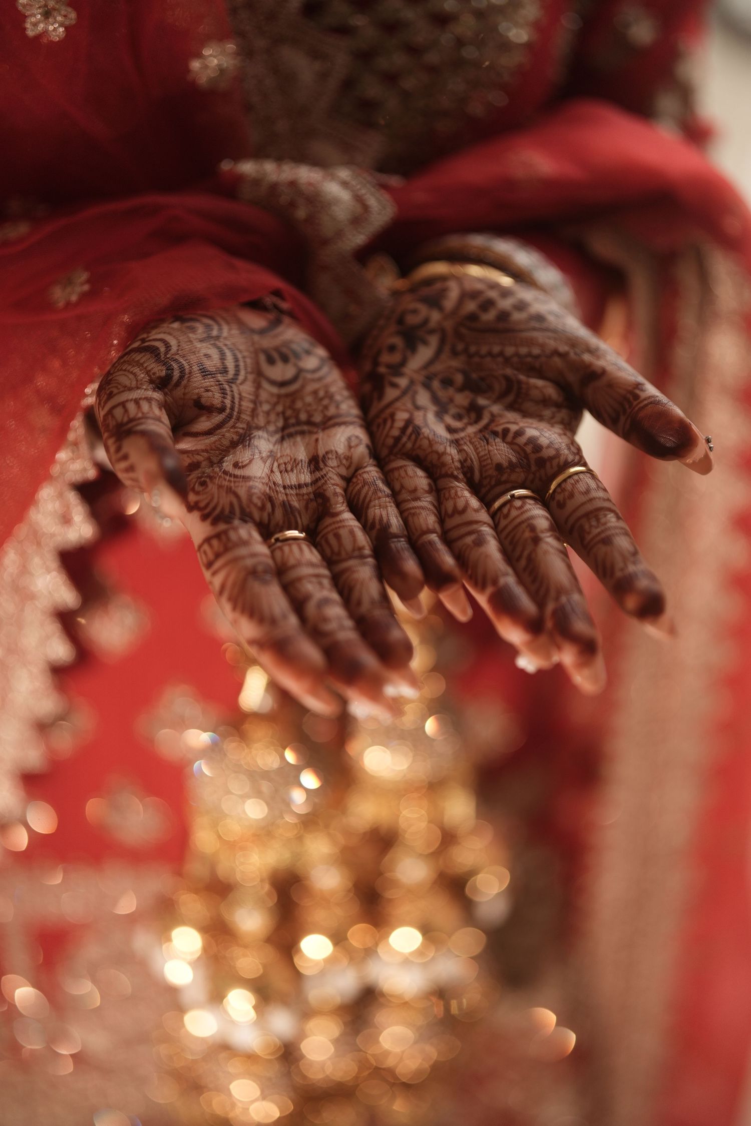 Indian bride displaying intricate mehndi henna designs on both palms with gold rings.