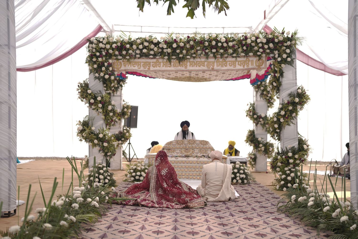 Elegant outdoor wedding mandap adorned with white and green floral arrangements under a draped canopy.
