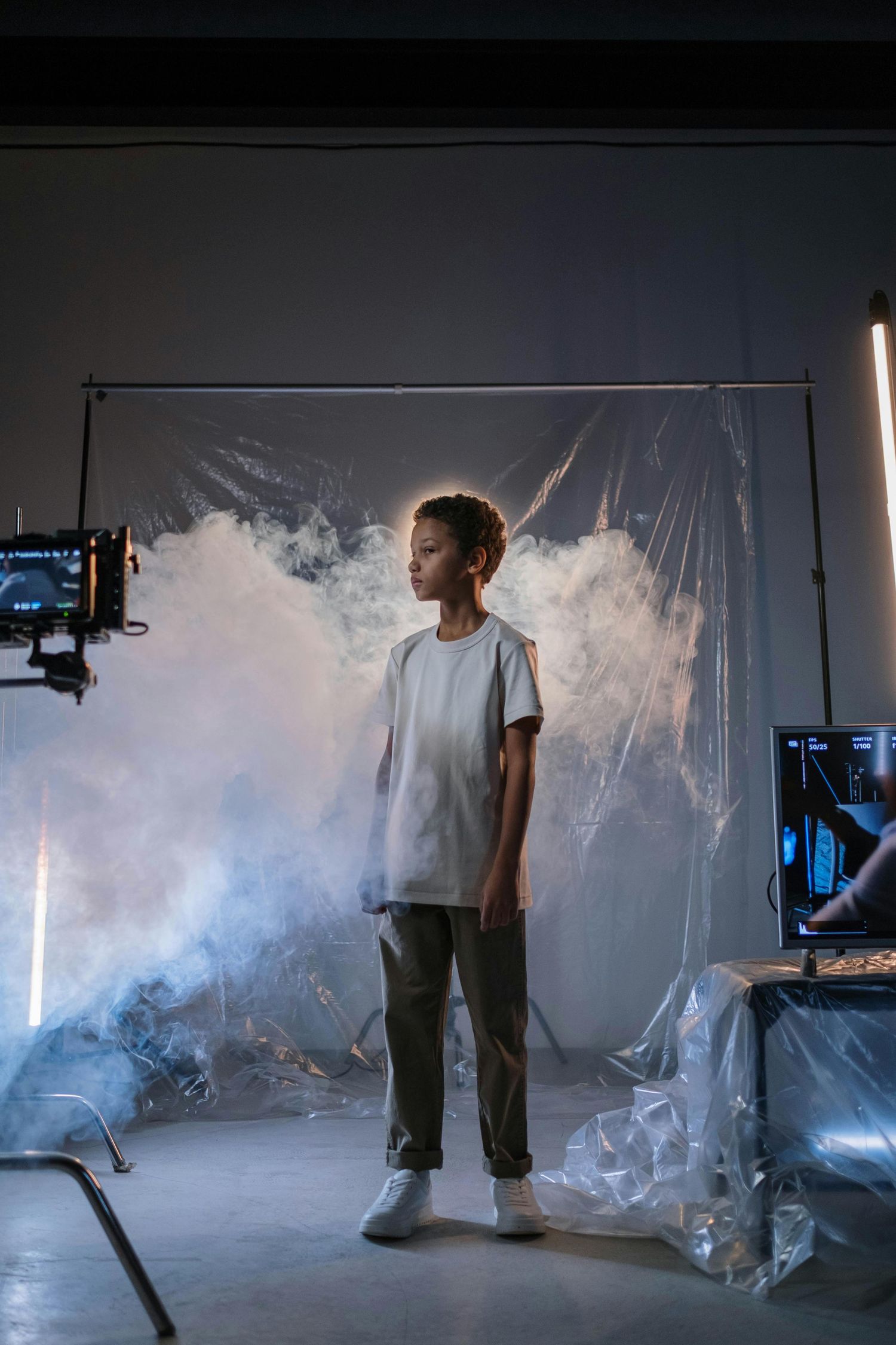 Young boy standing in dramatic smoke-filled photography studio with professional lighting equipment.
