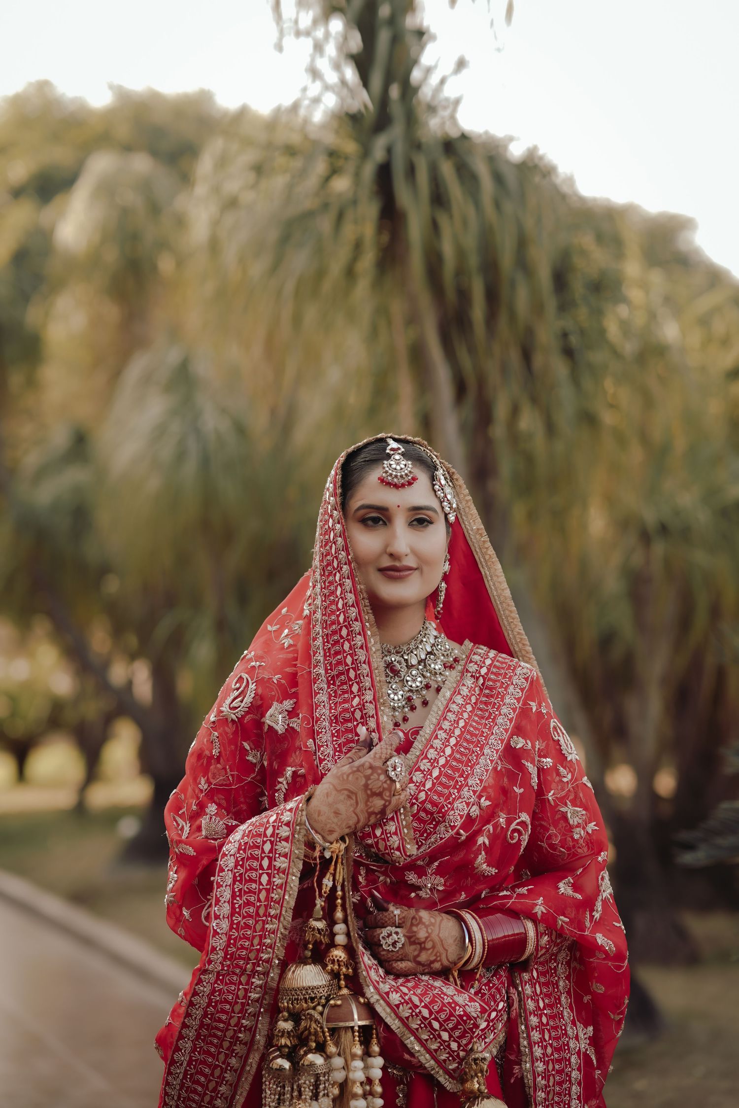 Indian Sikh bride in ornate red bridal lehenga with gold embroidery and traditional jewelry outdoors.