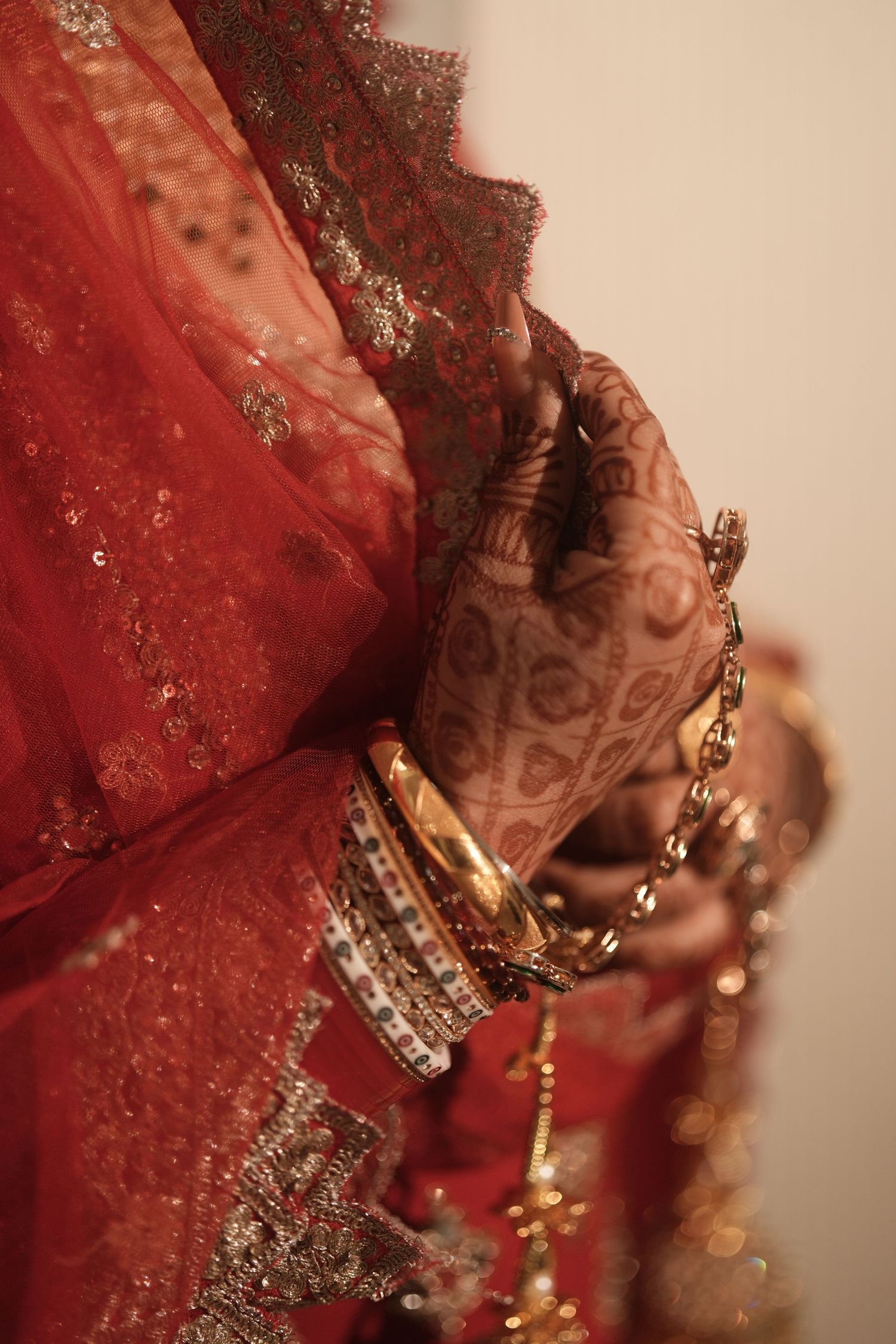 Close-up of Indian bride's mehndi hands with gold bangles and red bridal lehenga.