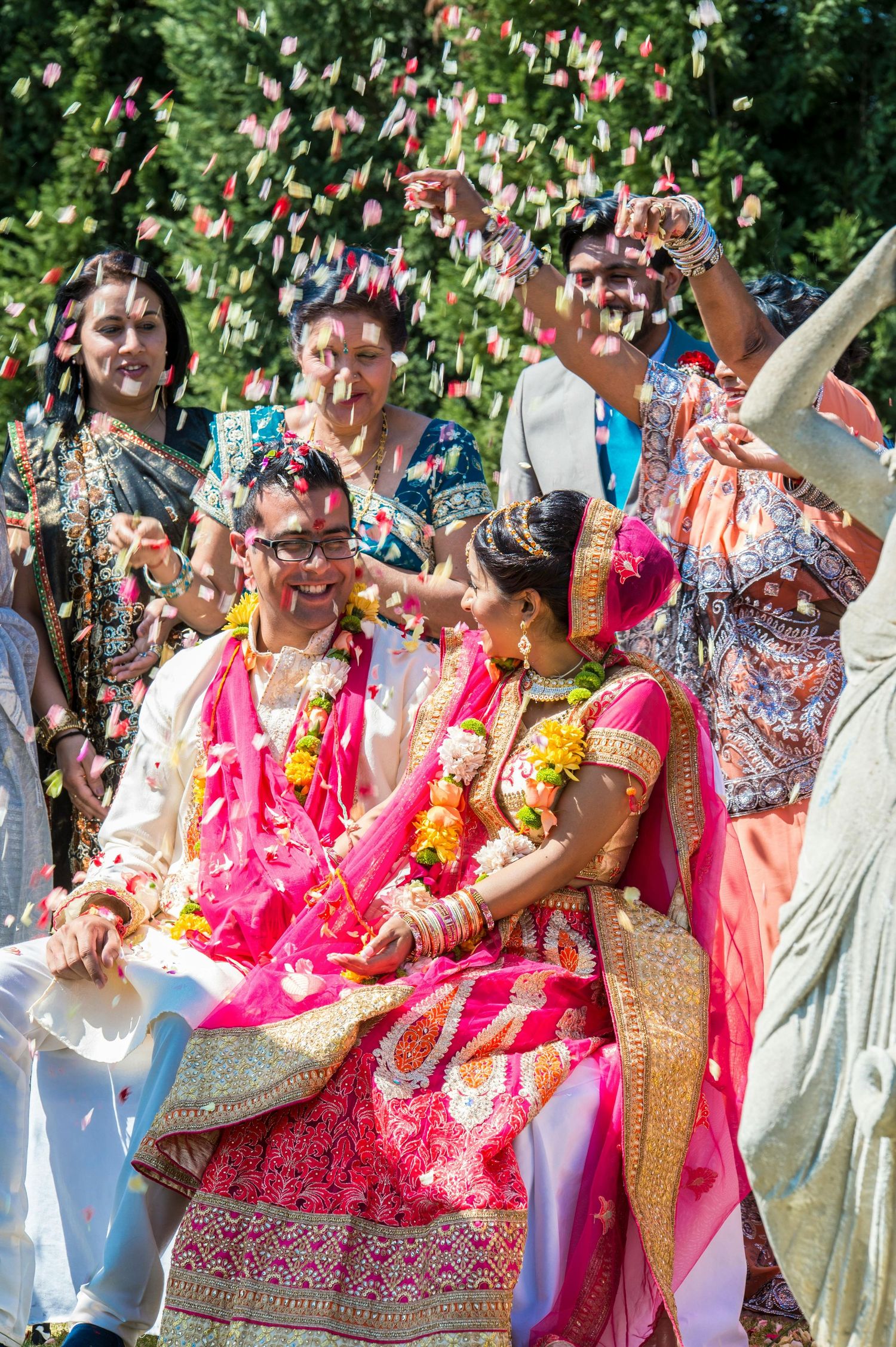 Joyful Indian wedding couple showered with flower petals during vibrant outdoor celebration ceremony.