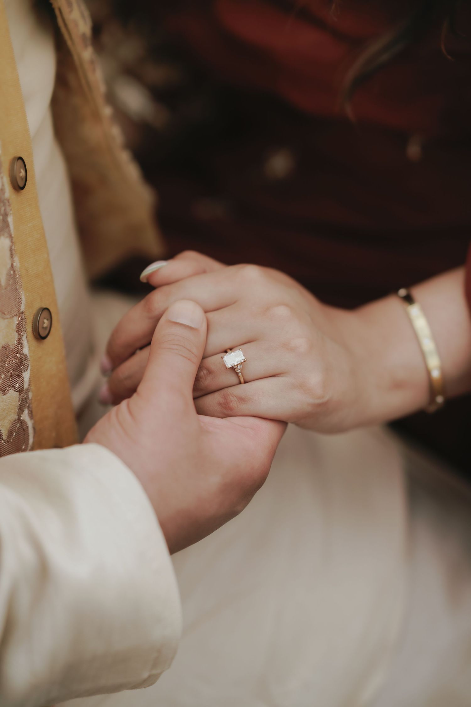 Close-up of a bride wearing a stunning emerald cut diamond engagement ring while holding her partners hand.