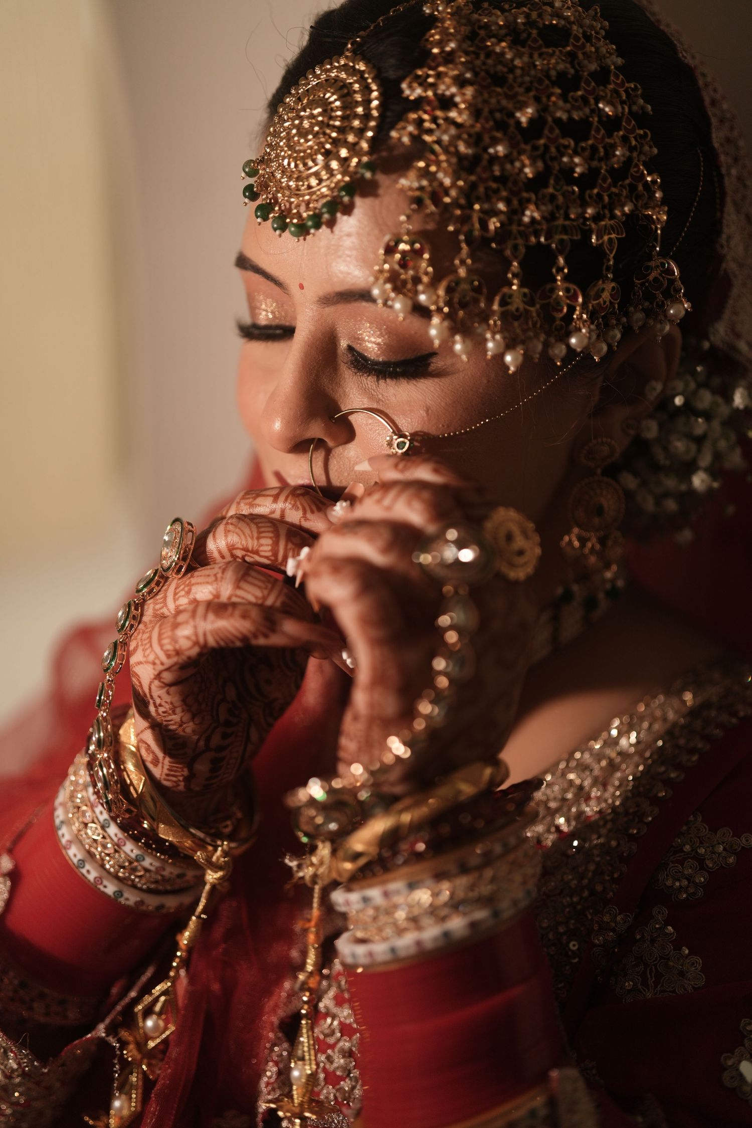 Indian bride with elaborate gold bridal jewelry and mehndi hands adjusting nose ring.