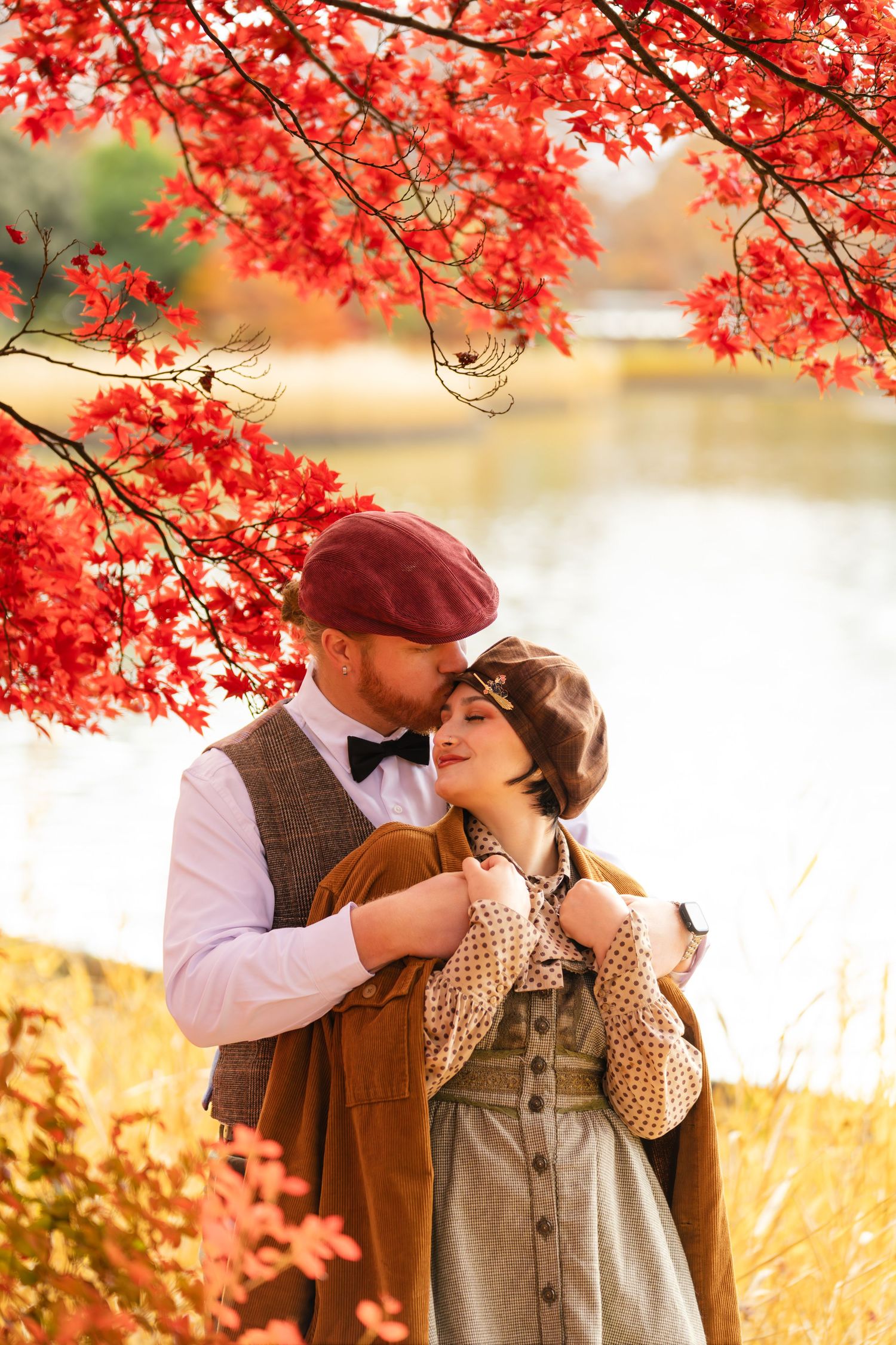 Romantic couple embracing under vibrant red autumn maple tree by a lake.