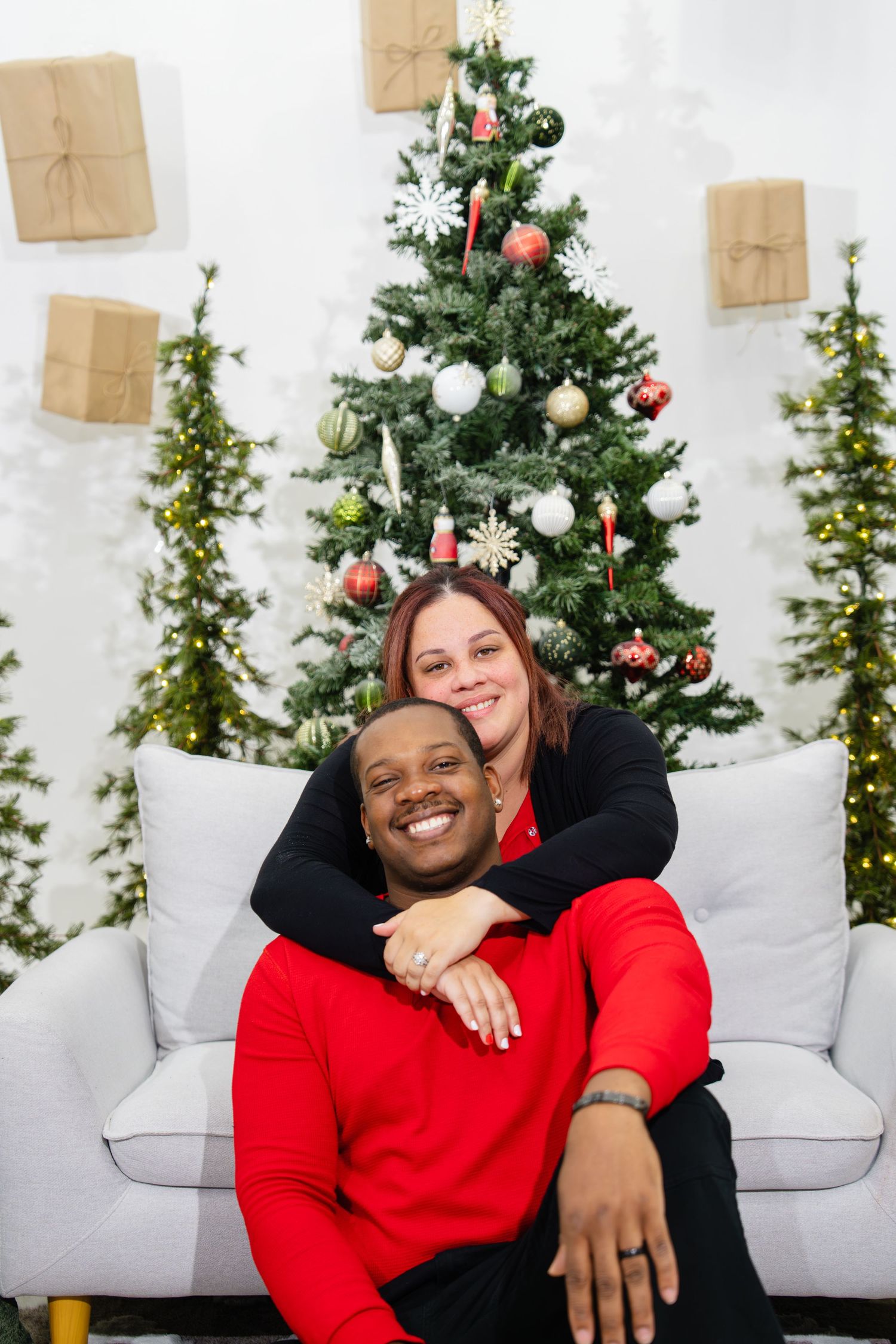 Smiling interracial couple posing together on a couch in front of a decorated Christmas tree.