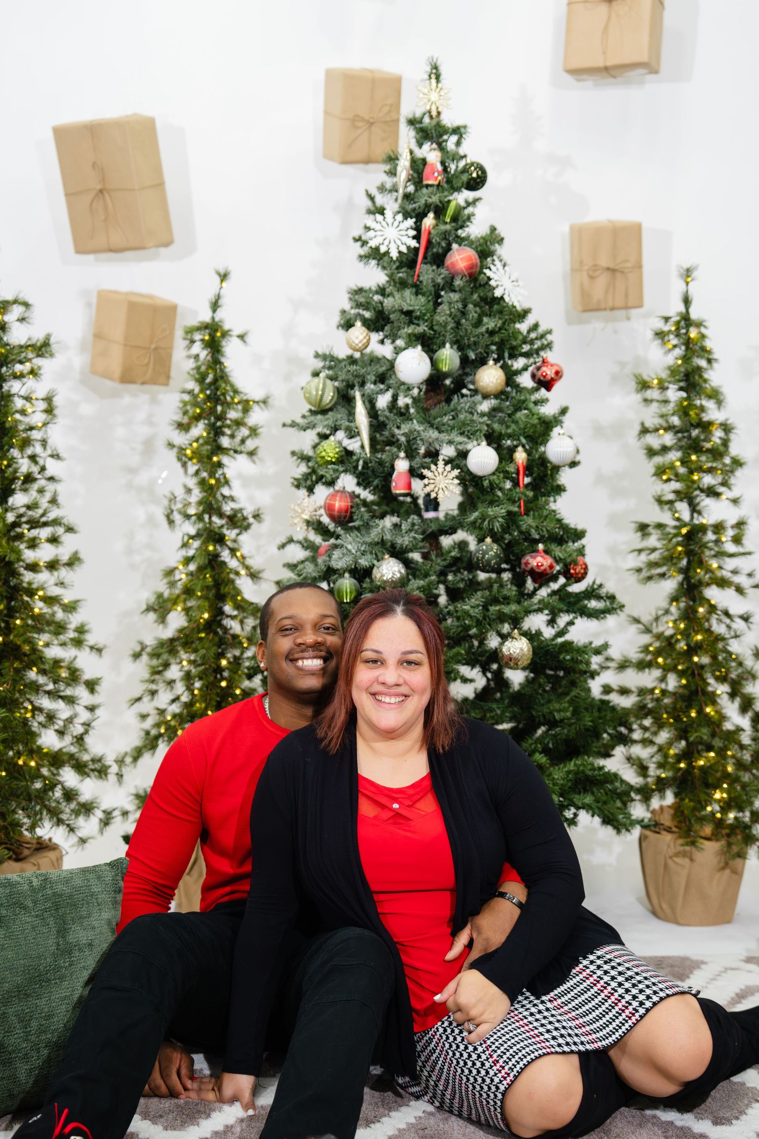 Happy interracial couple sitting together in front of a decorated Christmas tree with gift boxes.