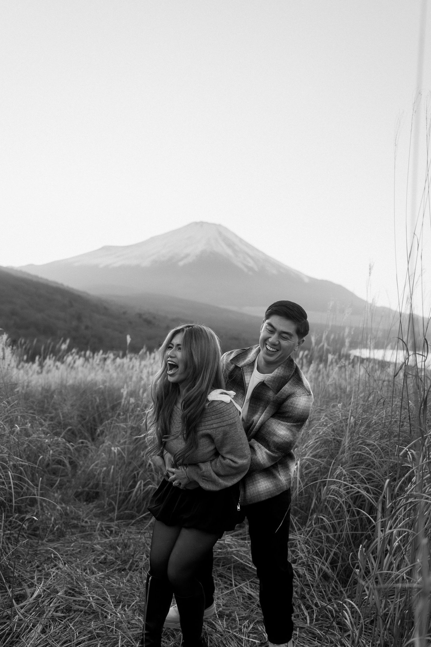 Joyful couple laughing together in a field with Mount Fuji in the background.
