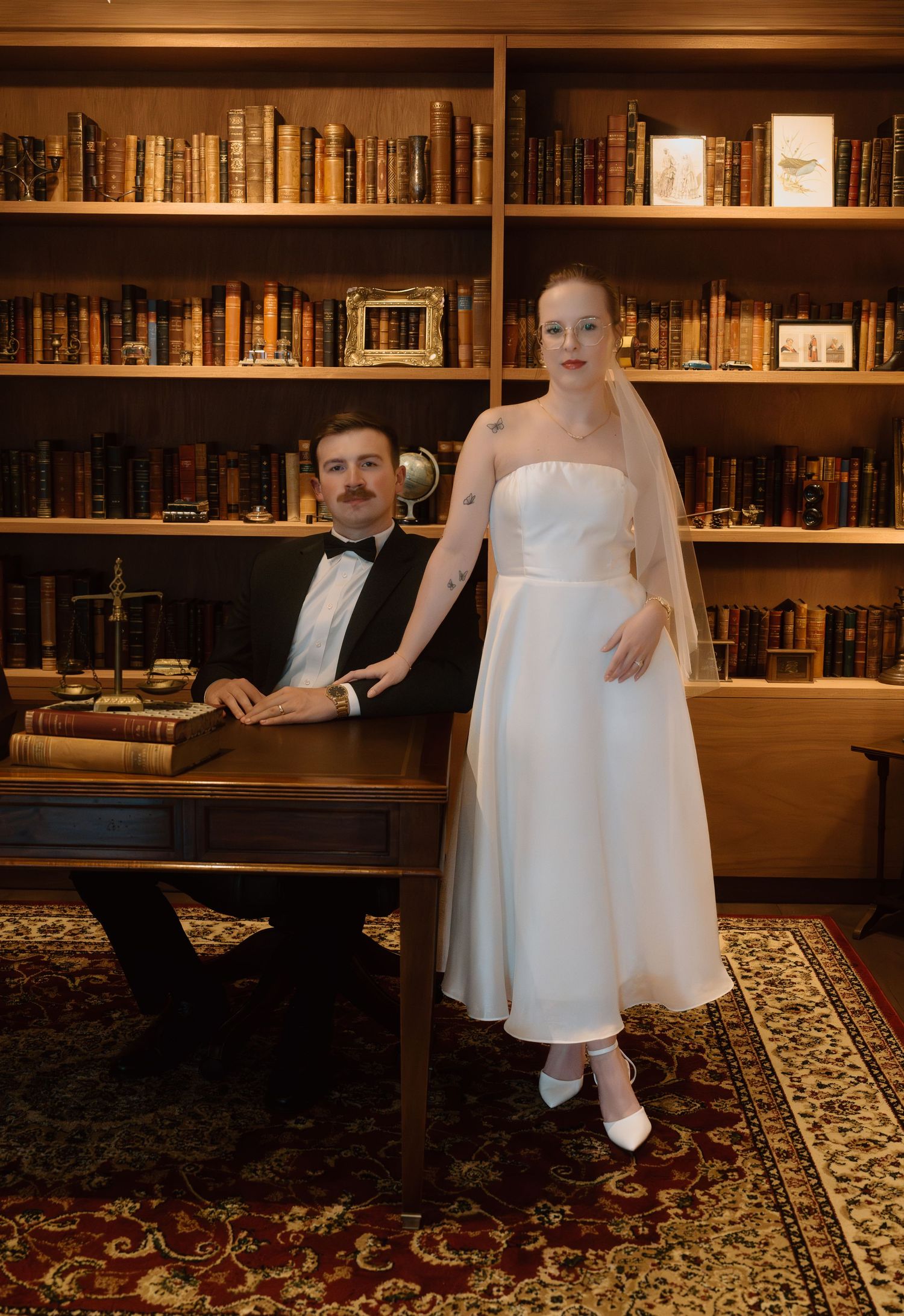 Elegant bride and groom posing in a classic library filled with antique books.