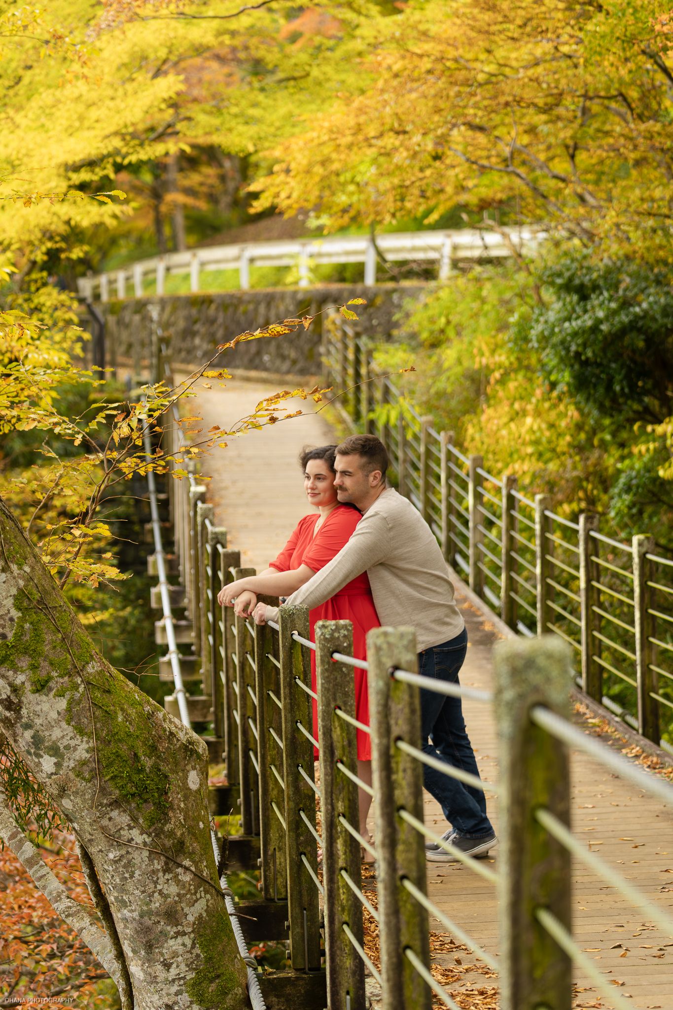 Couple standing on a wooden bridge surrounded by colorful autumn foliage.