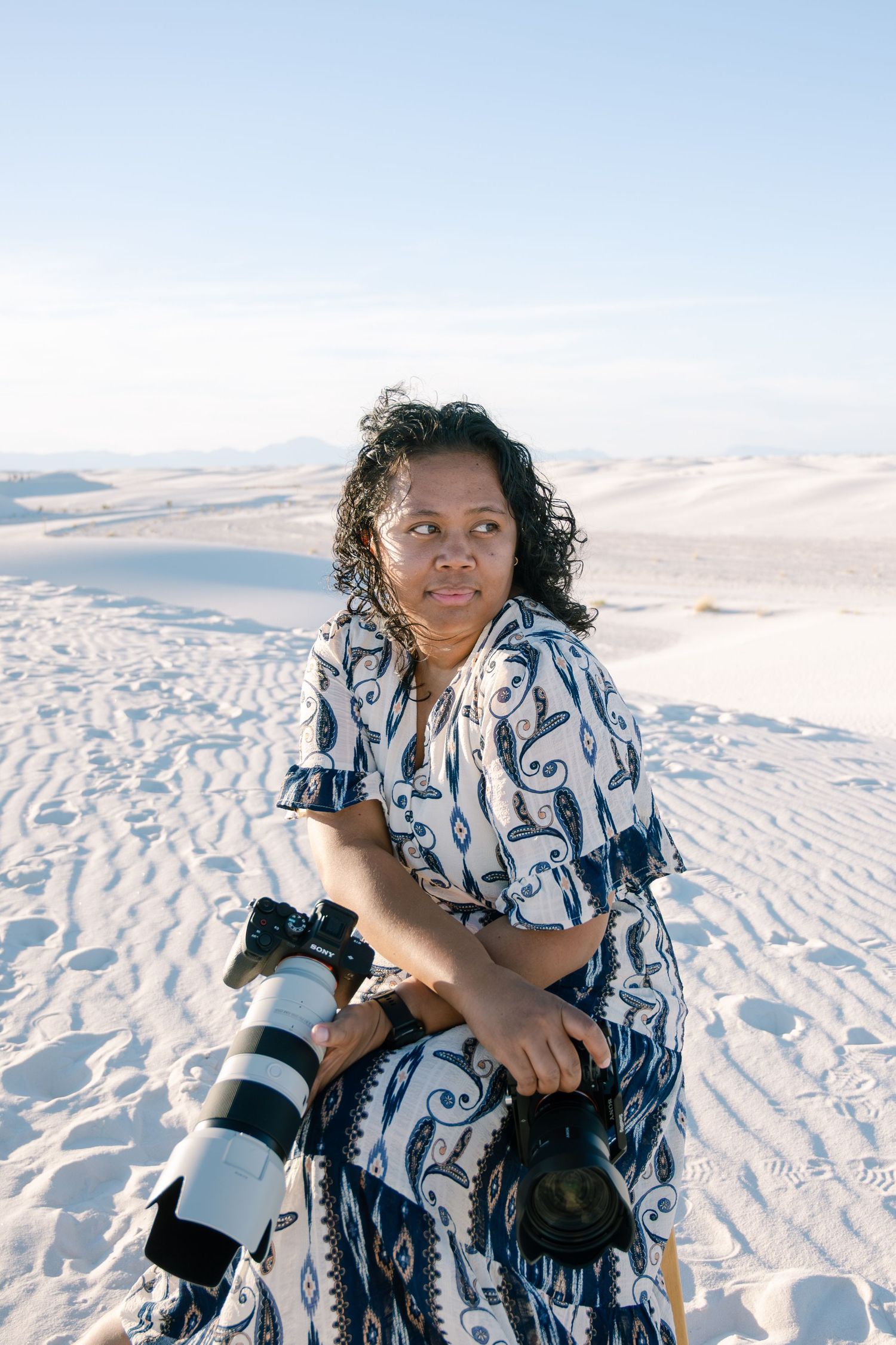 Female photographer with telephoto lens sitting on white sand dunes.