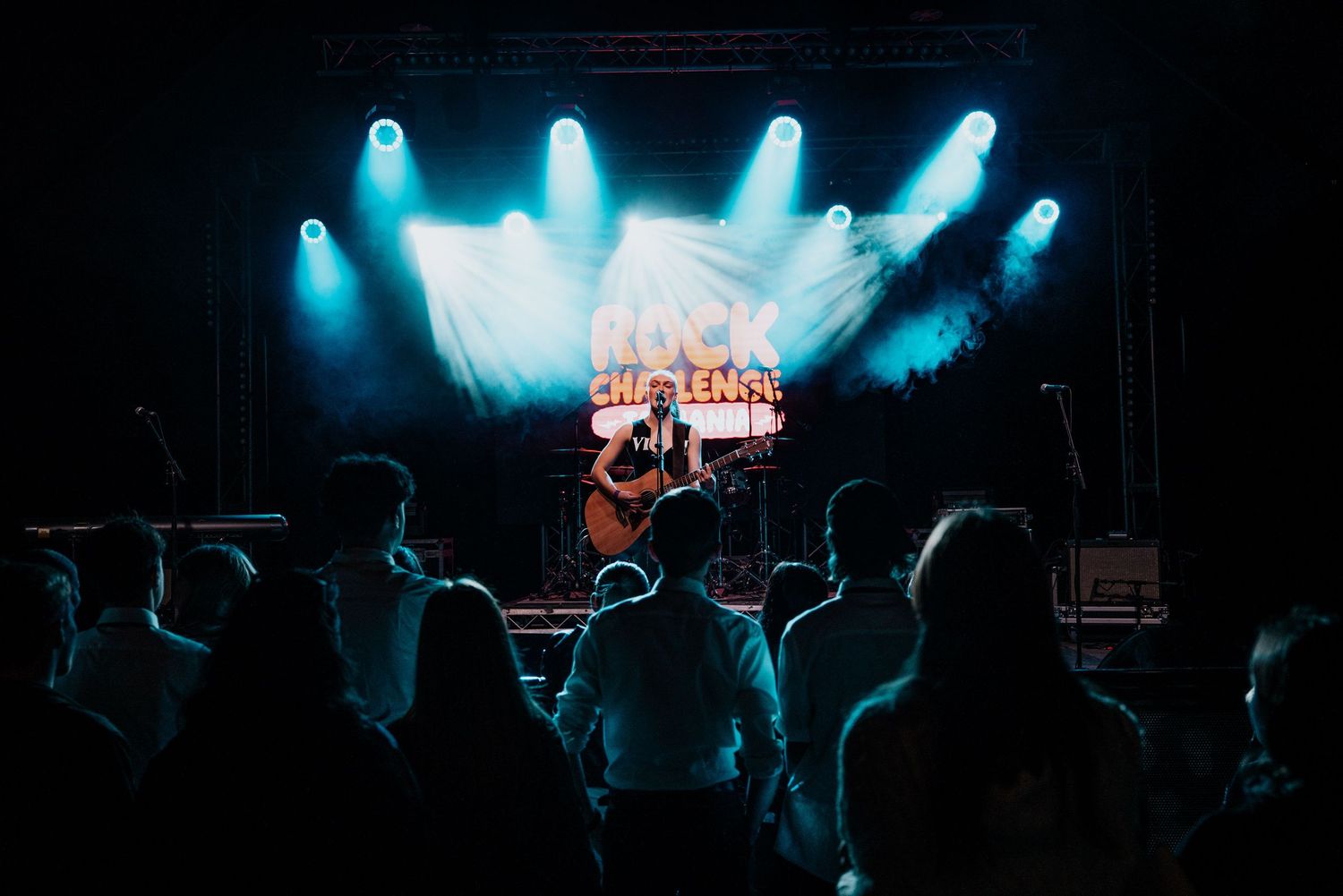 A solo guitarist performs on a lit stage at Rock Cheyenne festival before a silhouetted crowd.