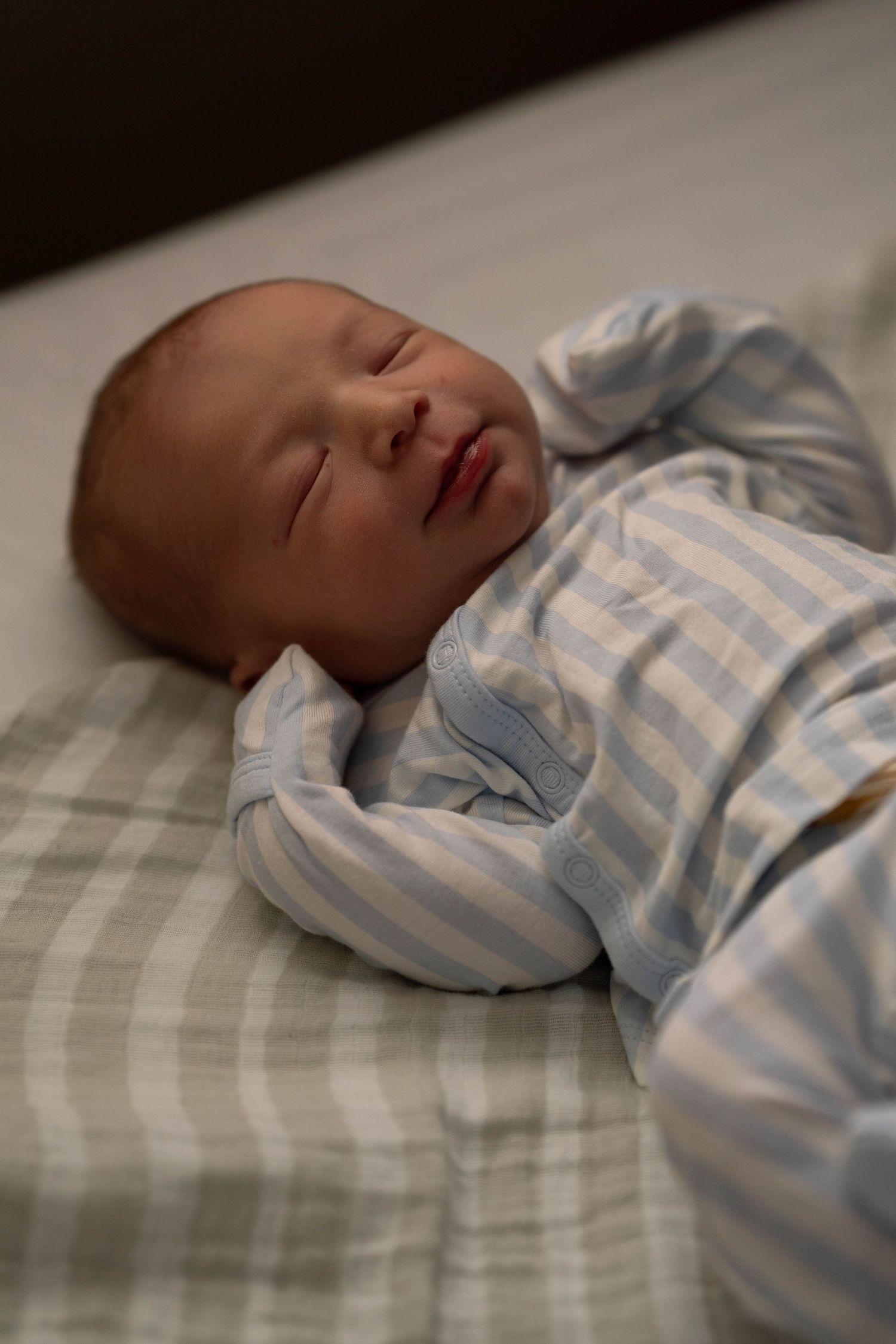 Peaceful newborn baby sleeping in blue striped onesie on soft white blanket.