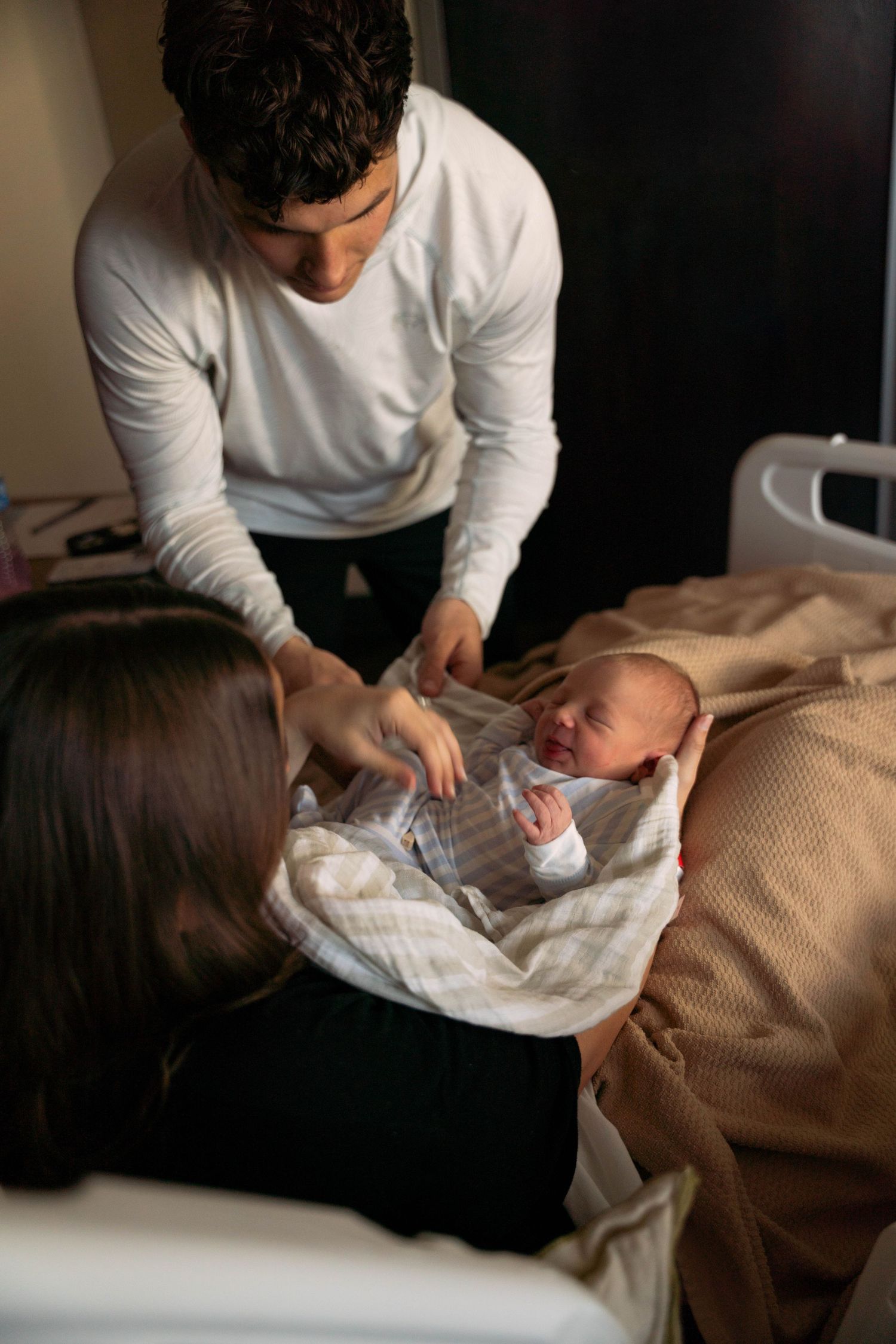 New parents in hospital room looking at swaddled crying newborn baby together.