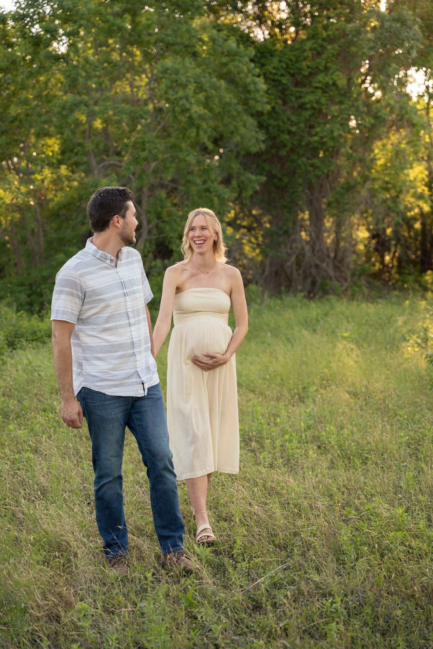 Happy pregnant couple walking together in a lush green field at golden hour.