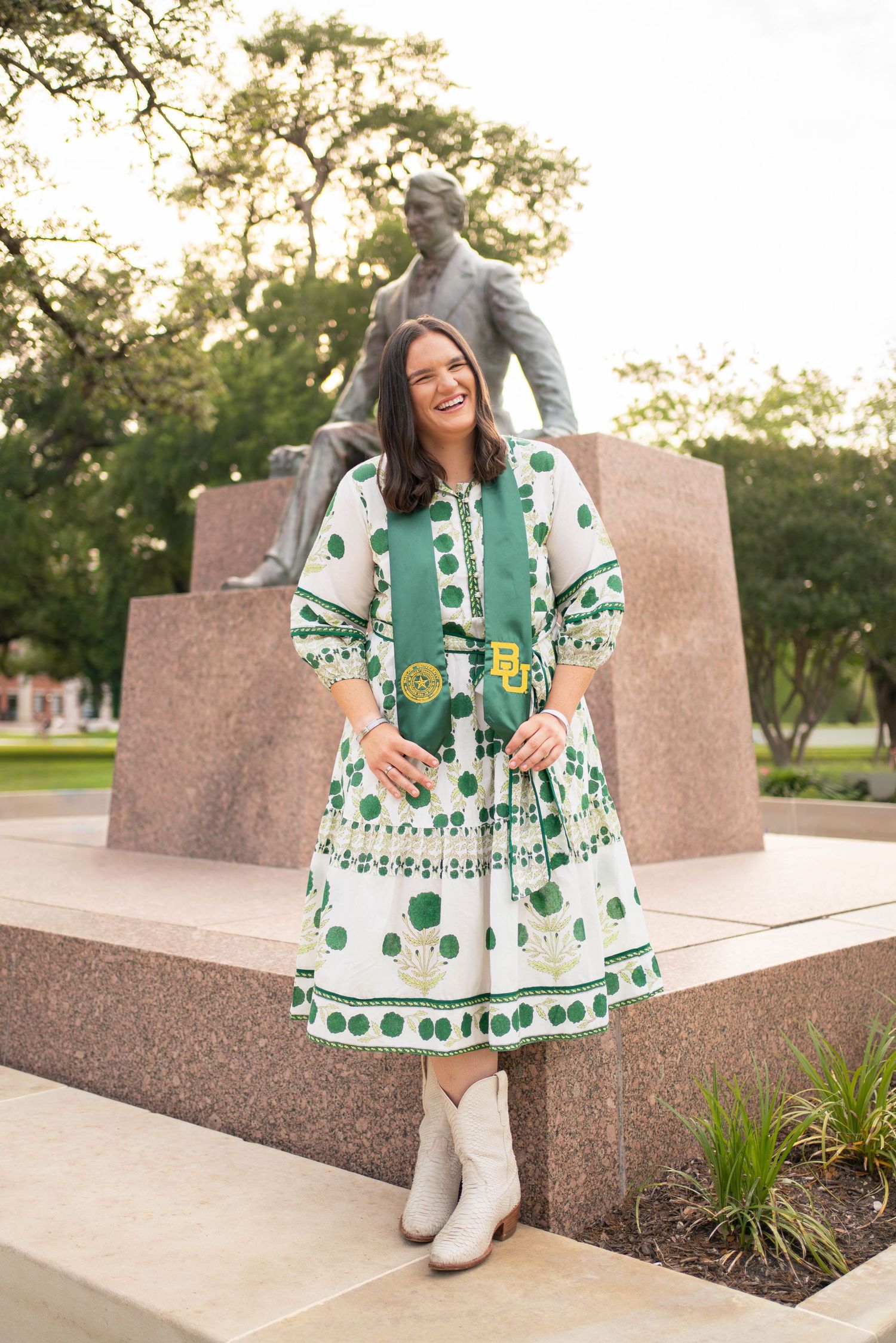 Baylor University graduate poses in green patterned dress with BU stole near campus statue.
