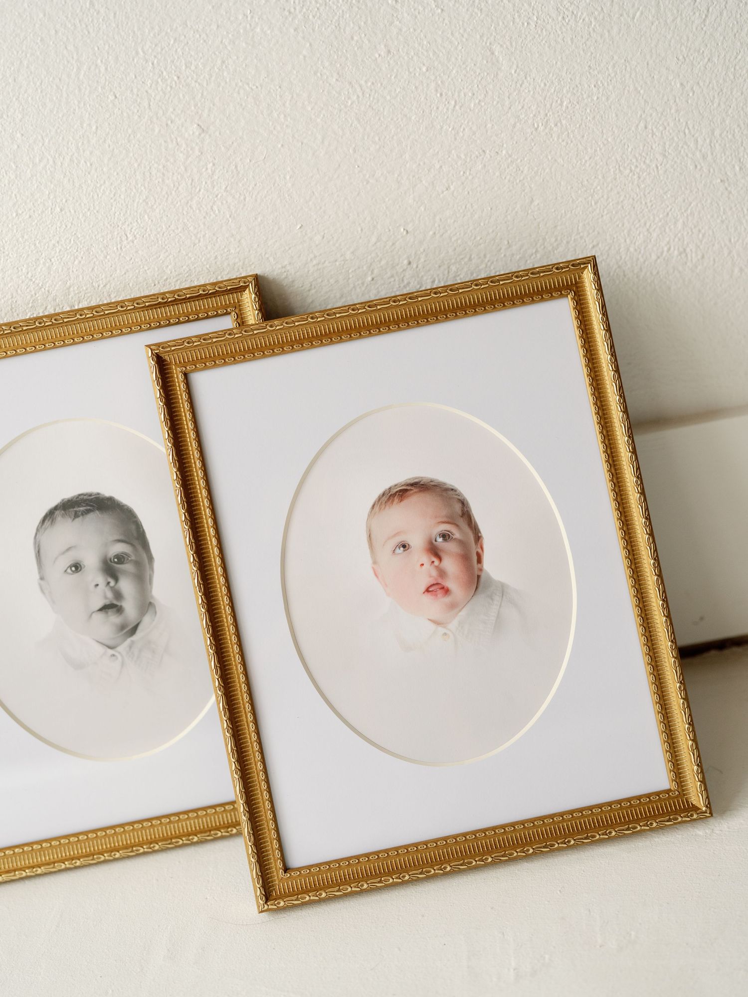 Two vintage gold-framed oval matted baby portraits displayed together, one black and white and one color photograph.