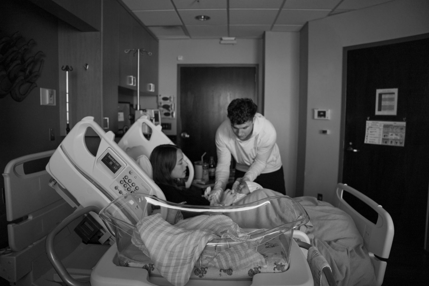 Black and white photo of new parents with newborn baby in hospital room after delivery.