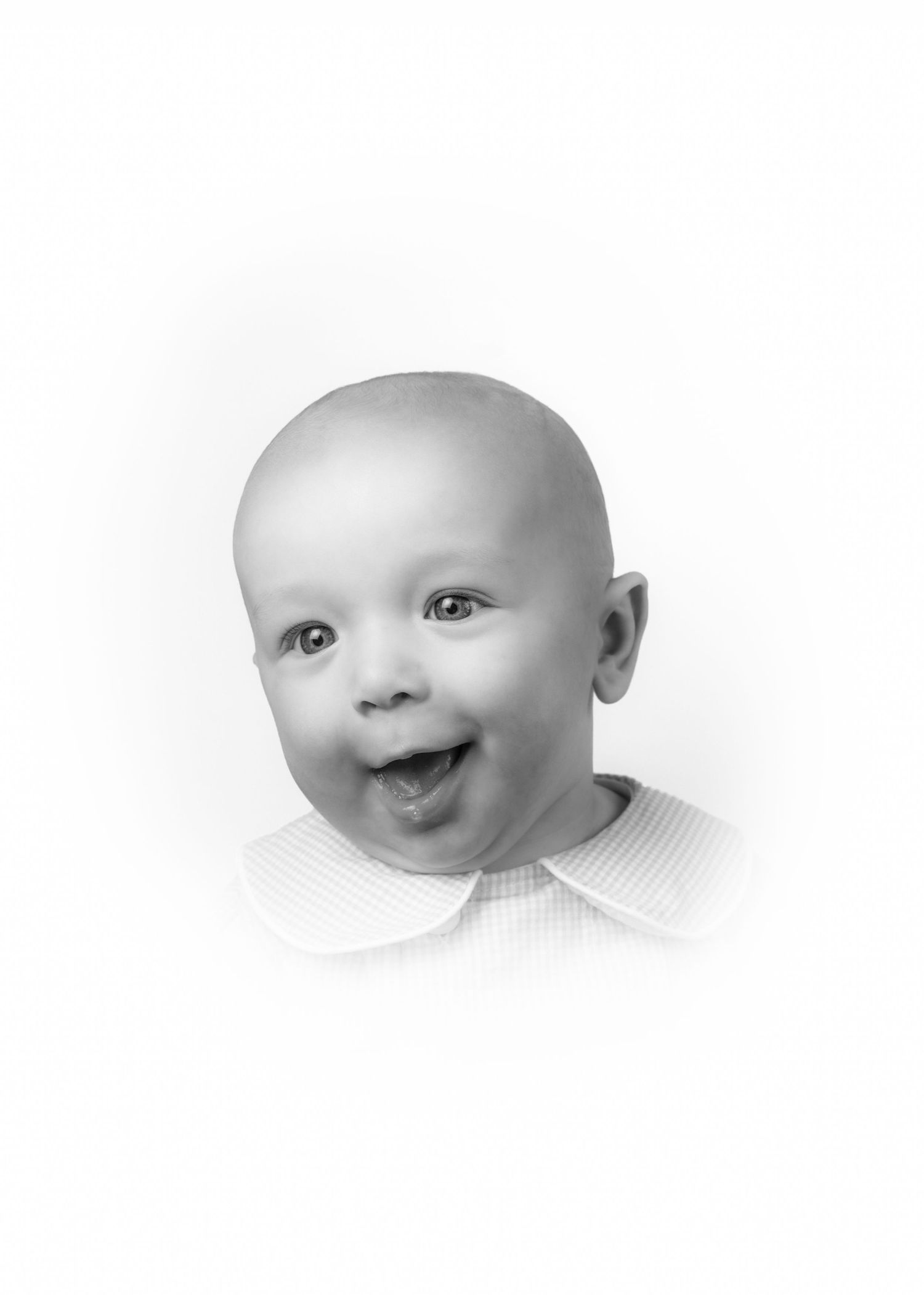 Black and white portrait of a happy smiling bald baby with mouth open, wearing a white collared outfit.
