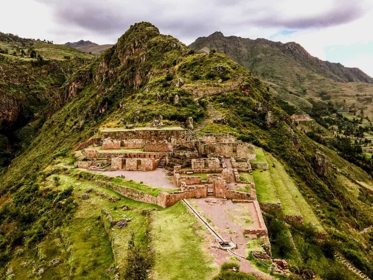 Aerial view of ancient Inca ruins nestled in lush green Andean mountains under cloudy skies in Peru.
