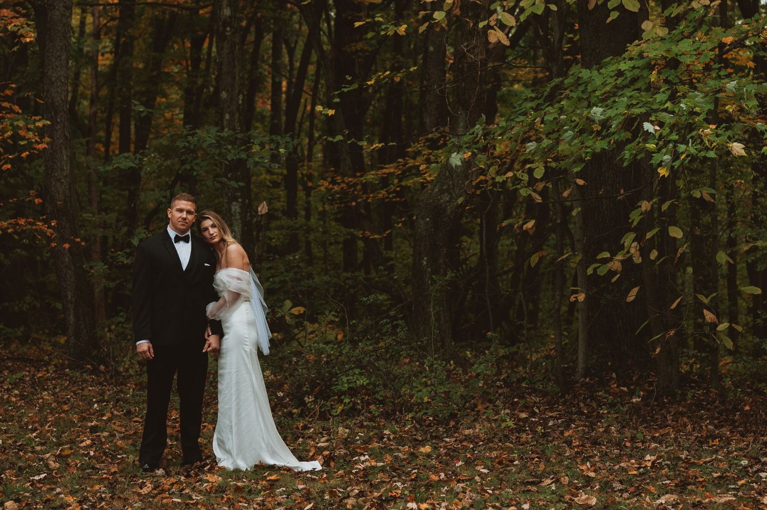 Bride and groom hold hands in an autumn forest with fallen leaves and colorful foliage.
