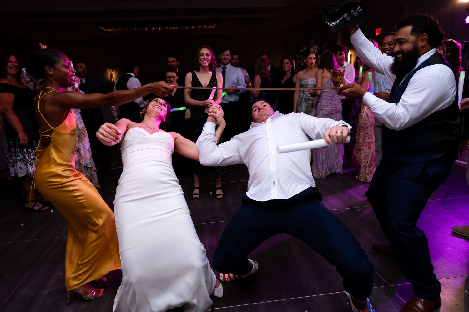 Bride and guests energetically dancing together on a purple-lit wedding reception dance floor.