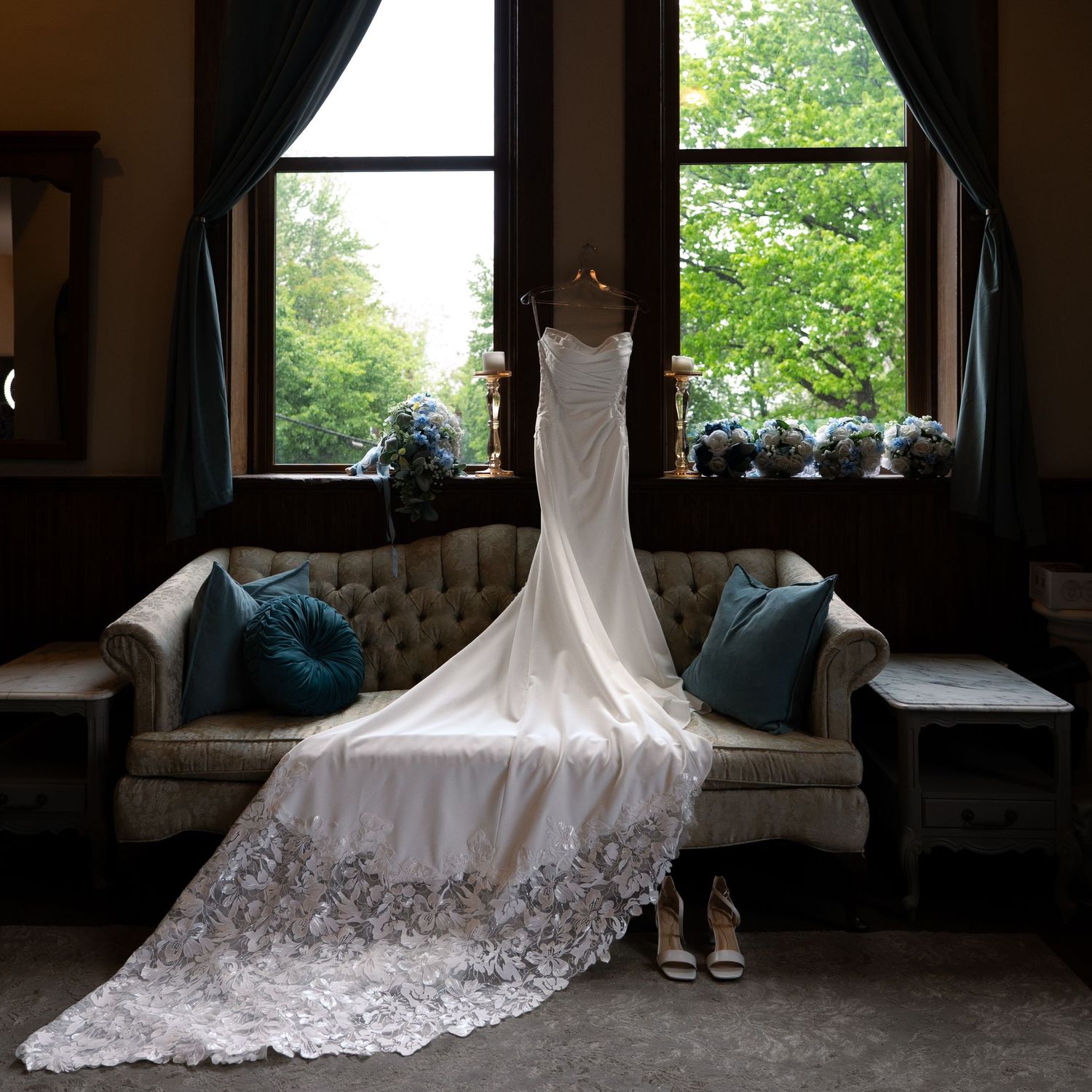 Elegant white lace wedding gown displayed on a vintage sofa near a sunlit window.