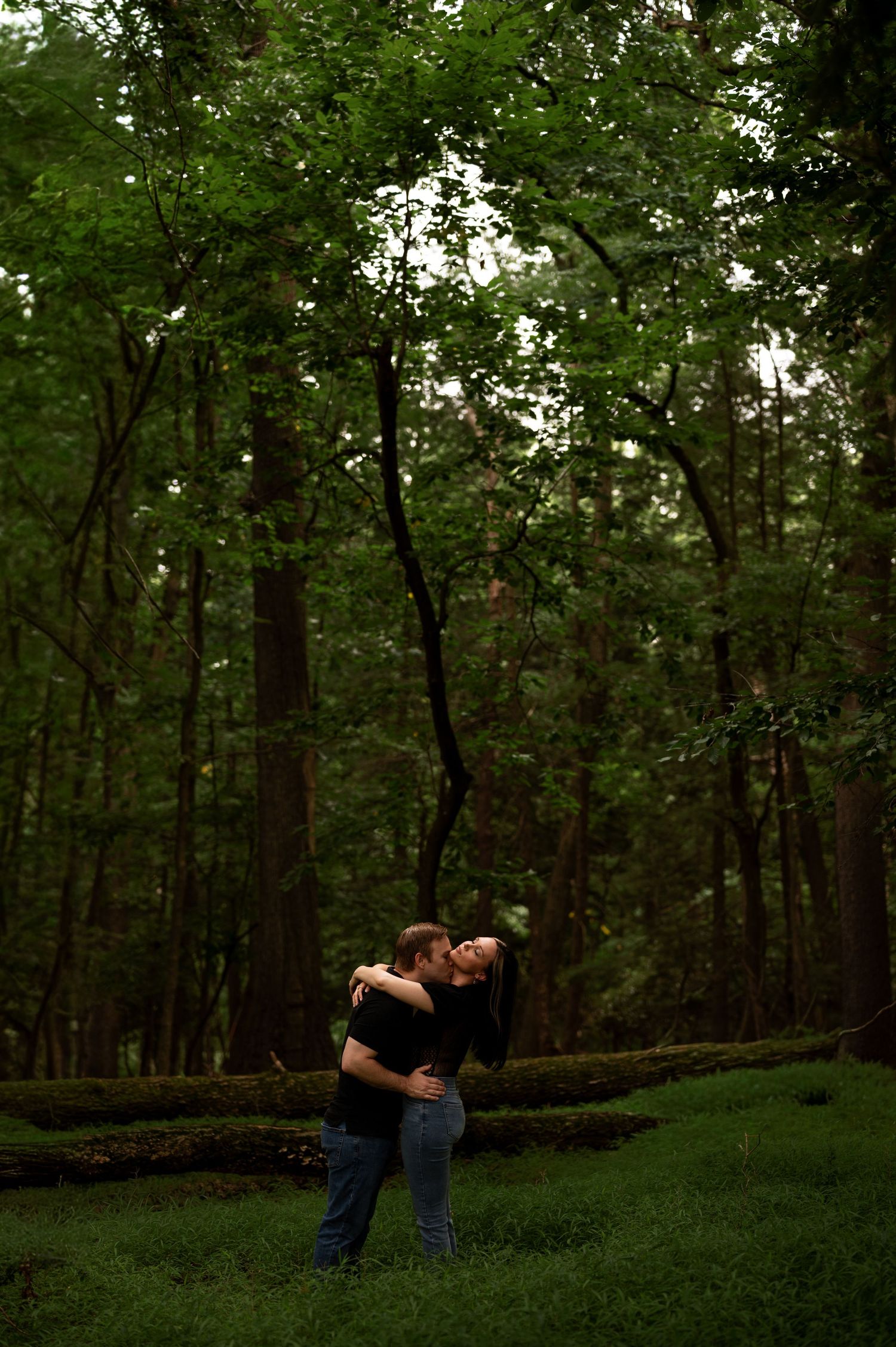 Couple sharing a romantic kiss in a lush green forest during an engagement photo session.