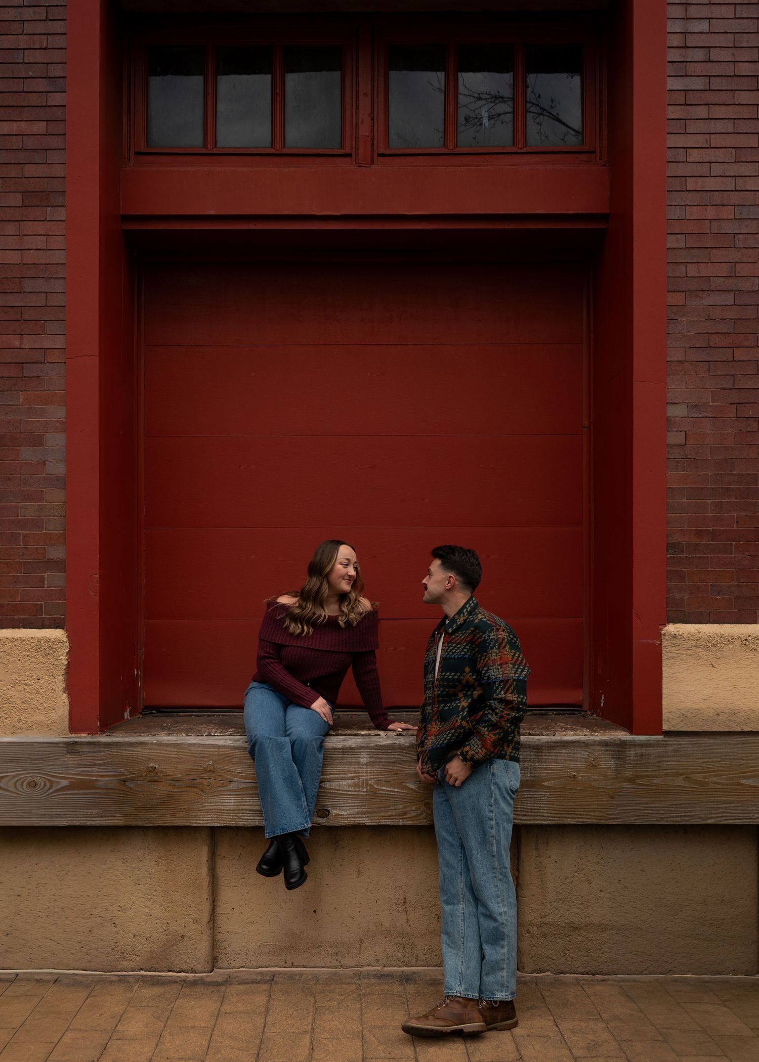 Happy couple laughs together in front of a red brick building during engagement photos.