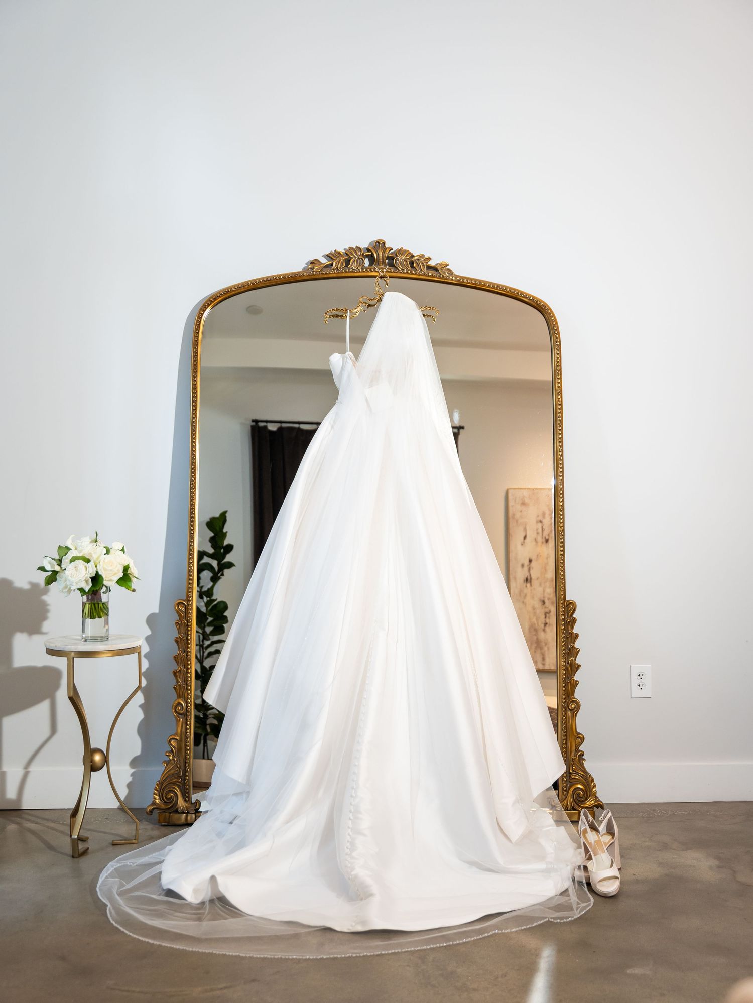 Wedding dress hanging in front of an ornate mirror before the ceremony.