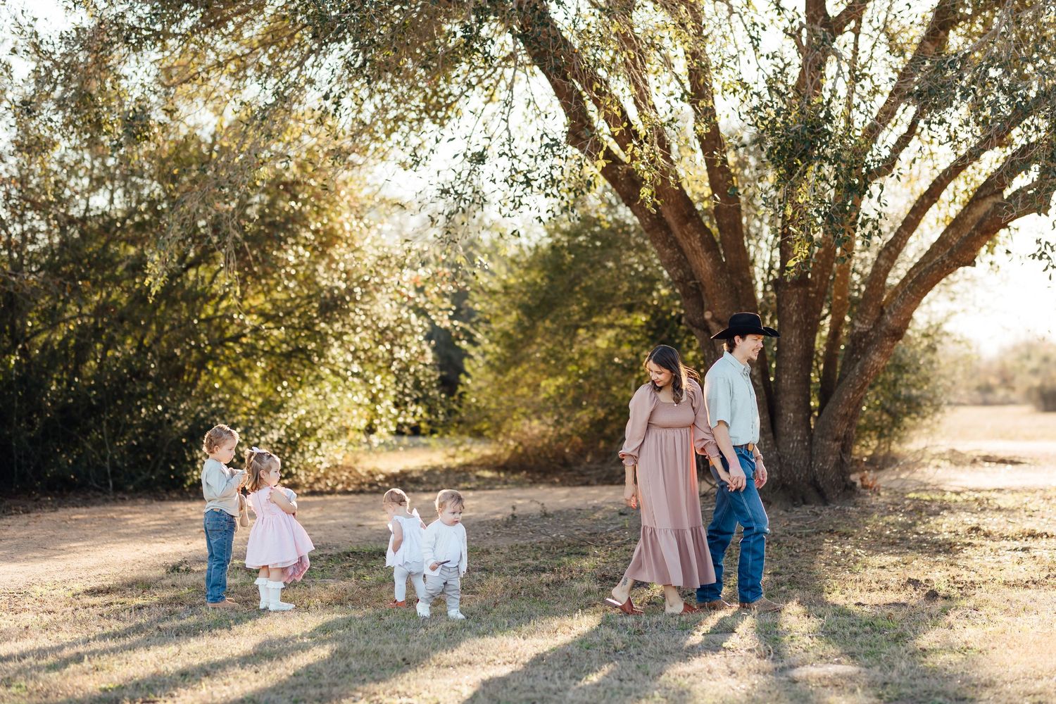 A family gathers under a sun-dappled tree on a warm afternoon while children play in soft natural light.