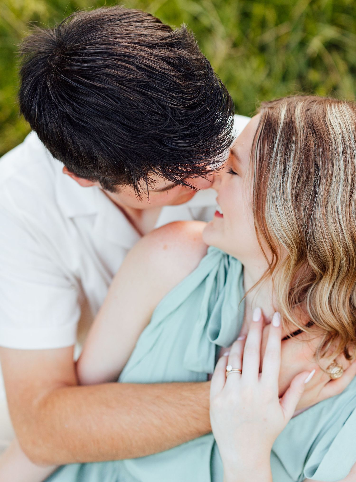 A romantic couple share a tender moment outdoors, dressed in white and mint green clothing.