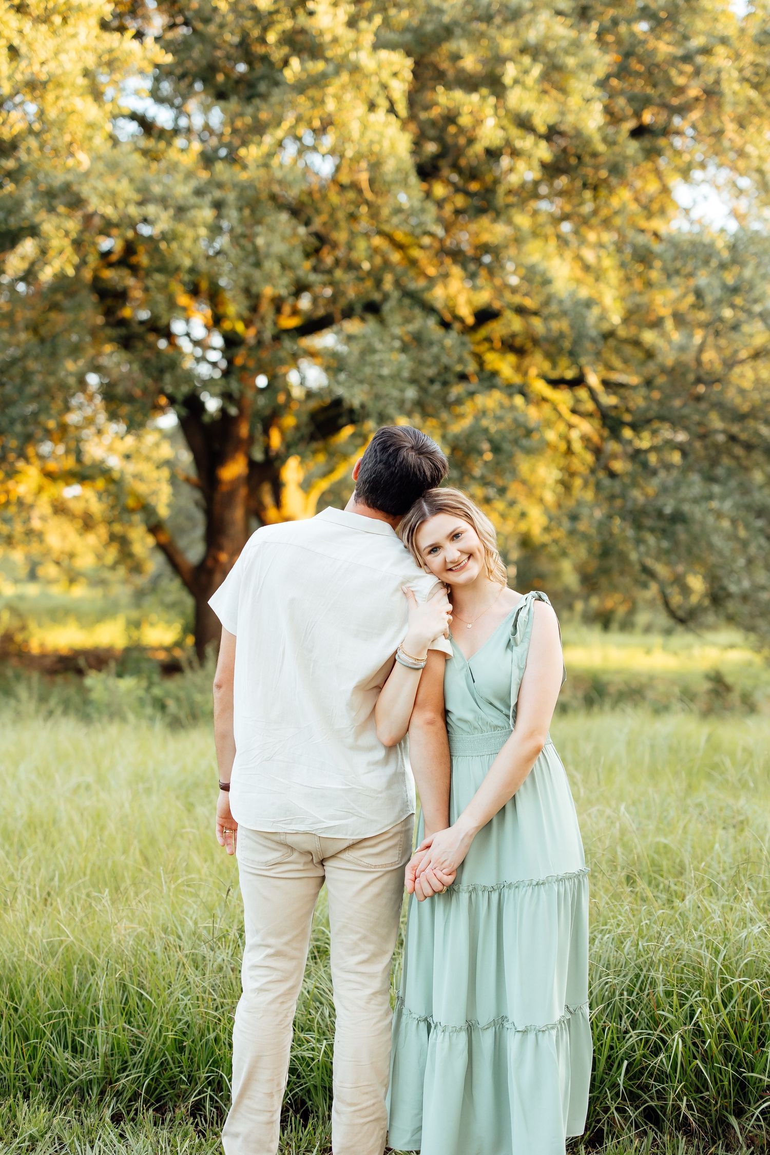 A couple shares a tender moment in a sunny park with golden trees and grass in the background.