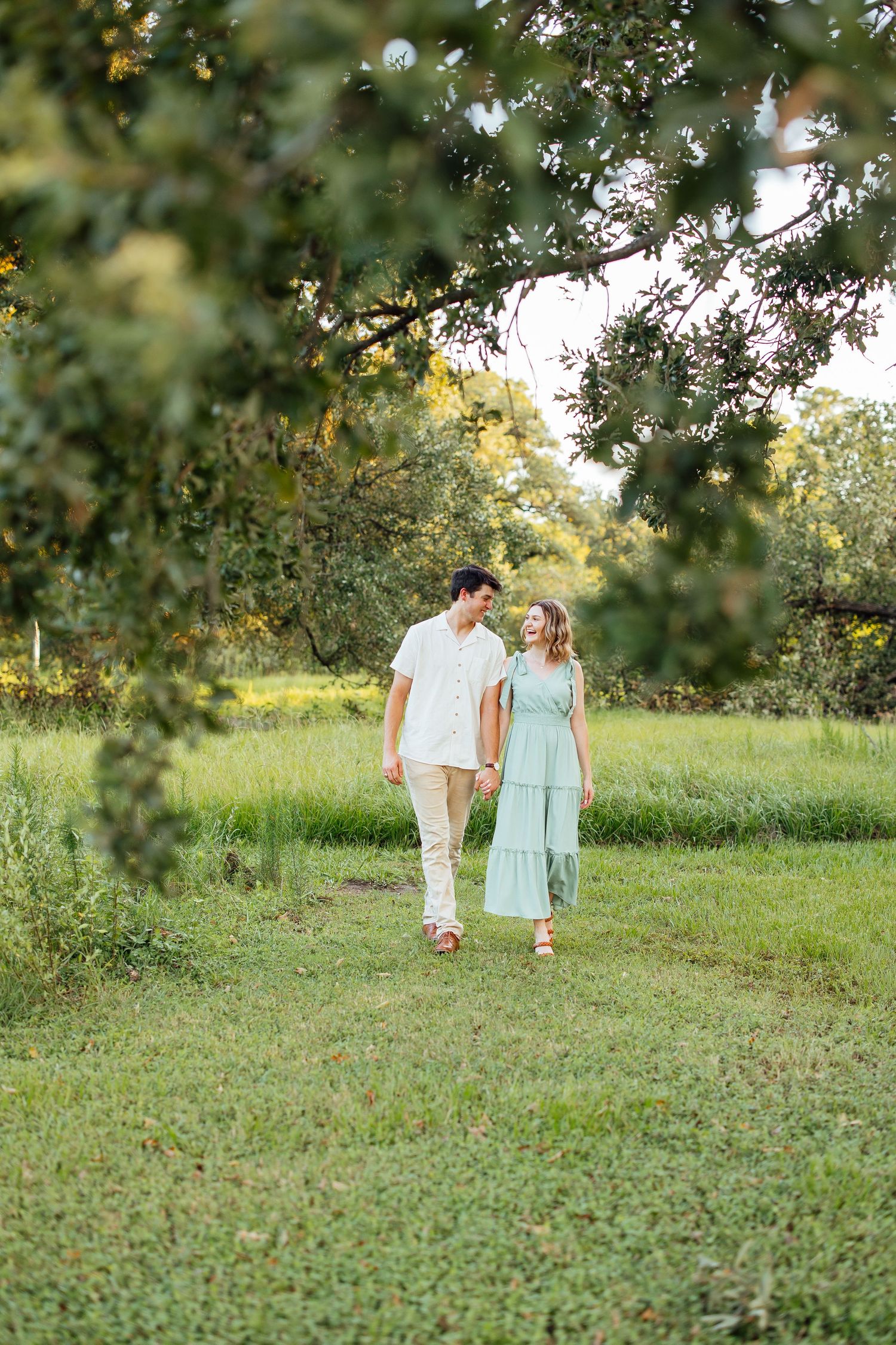 A couple walking together through a sunlit orchard on a summer afternoon, wearing white and mint green outfits.