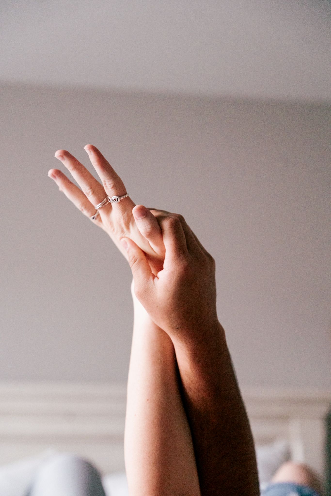 Close-up of two hands raised together showing delicate silver stacking rings on woman's fingers.