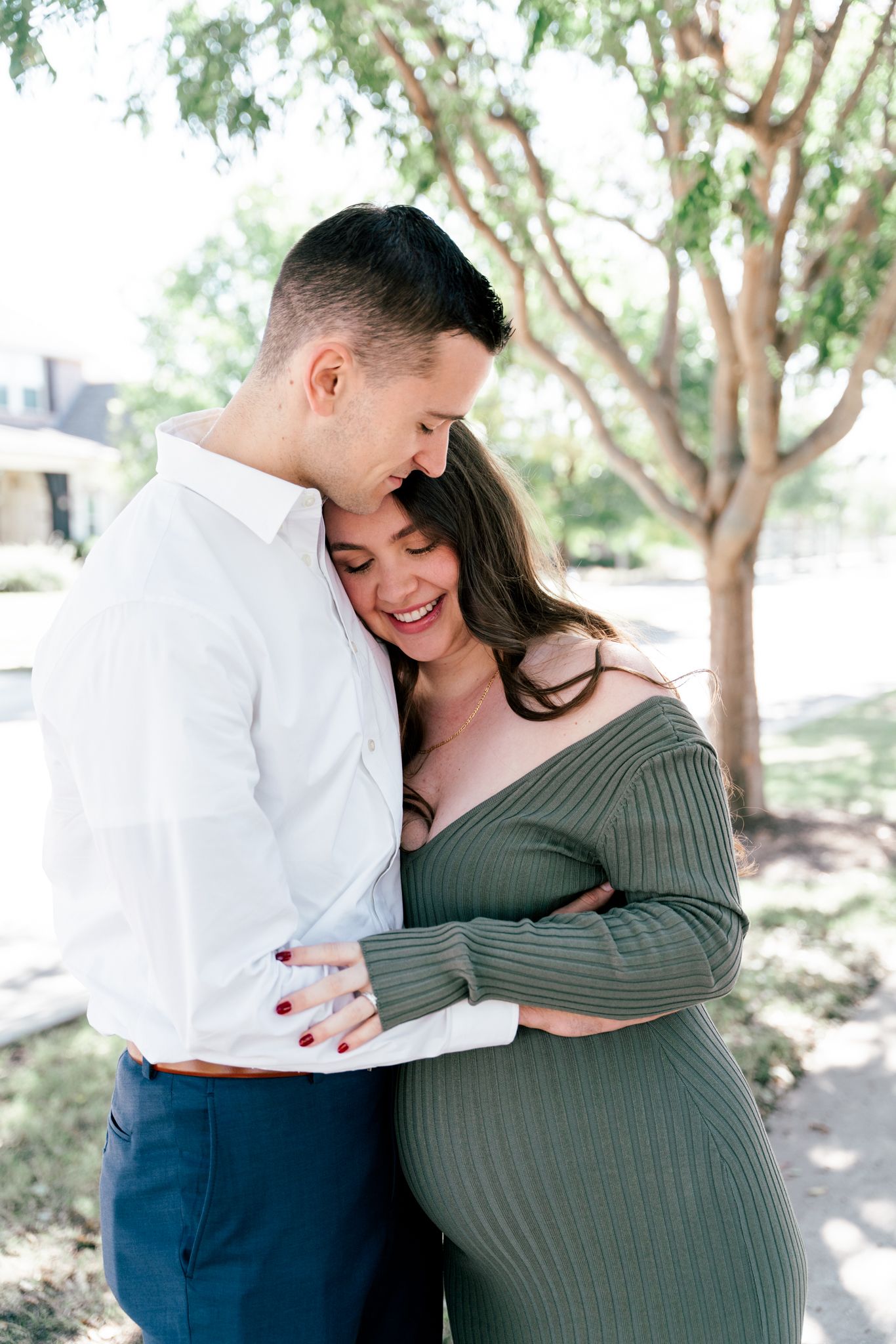 Happy couple embracing and laughing together outdoors under shaded trees.