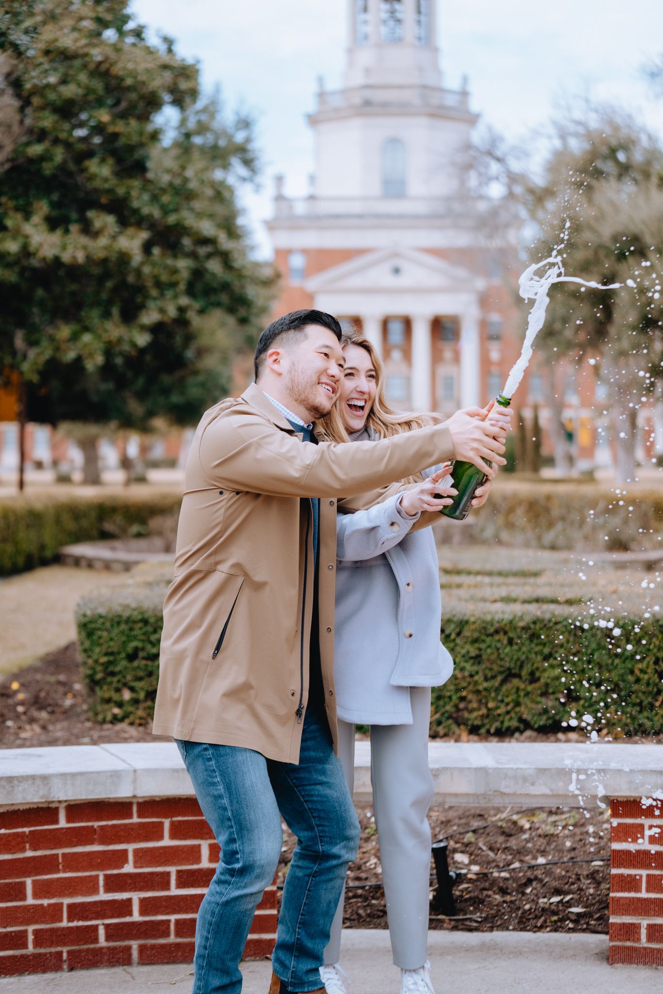 Happy couple popping champagne bottle outside historic building.
