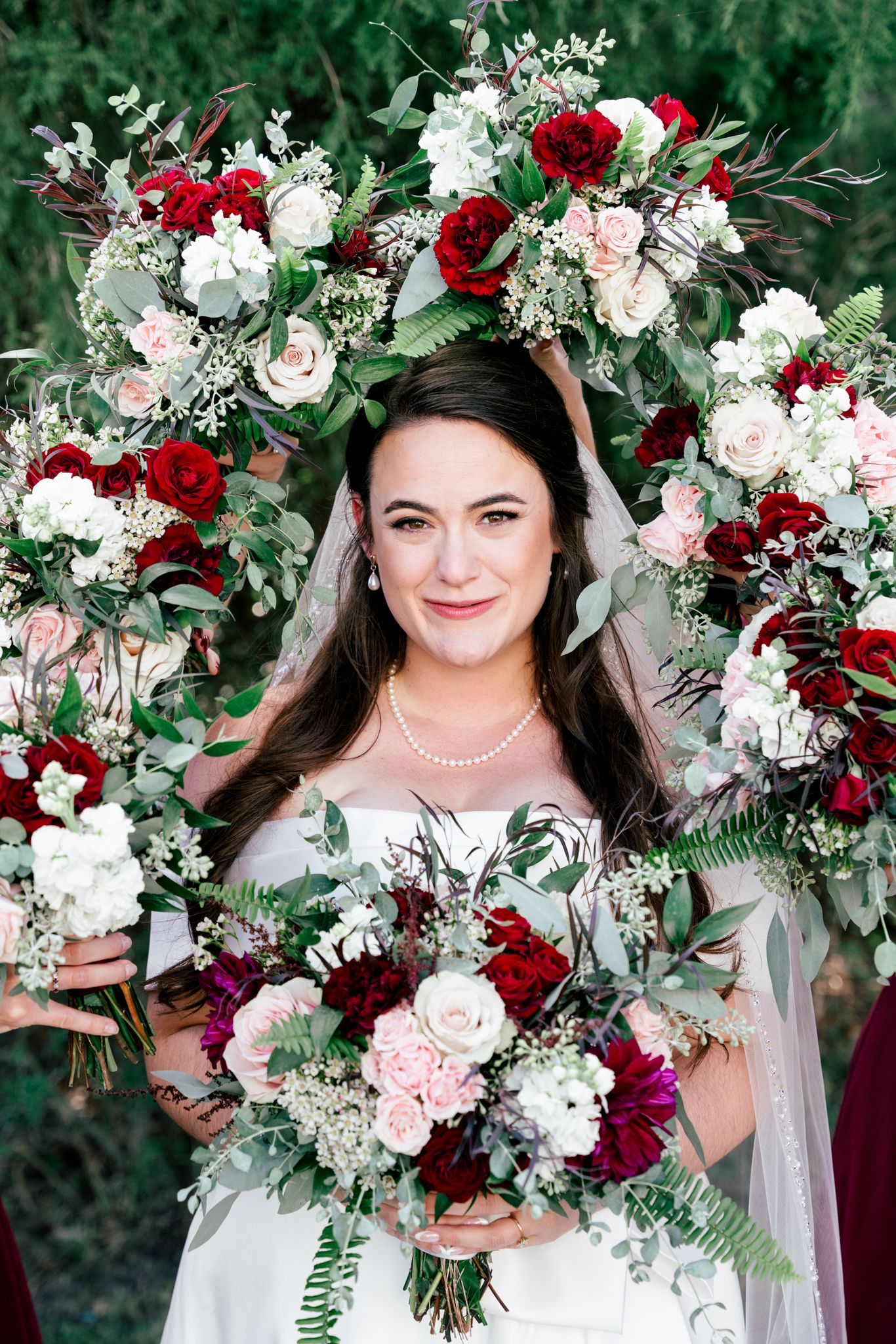 Bride surrounded by bridesmaids holding lush red and white floral bouquets.