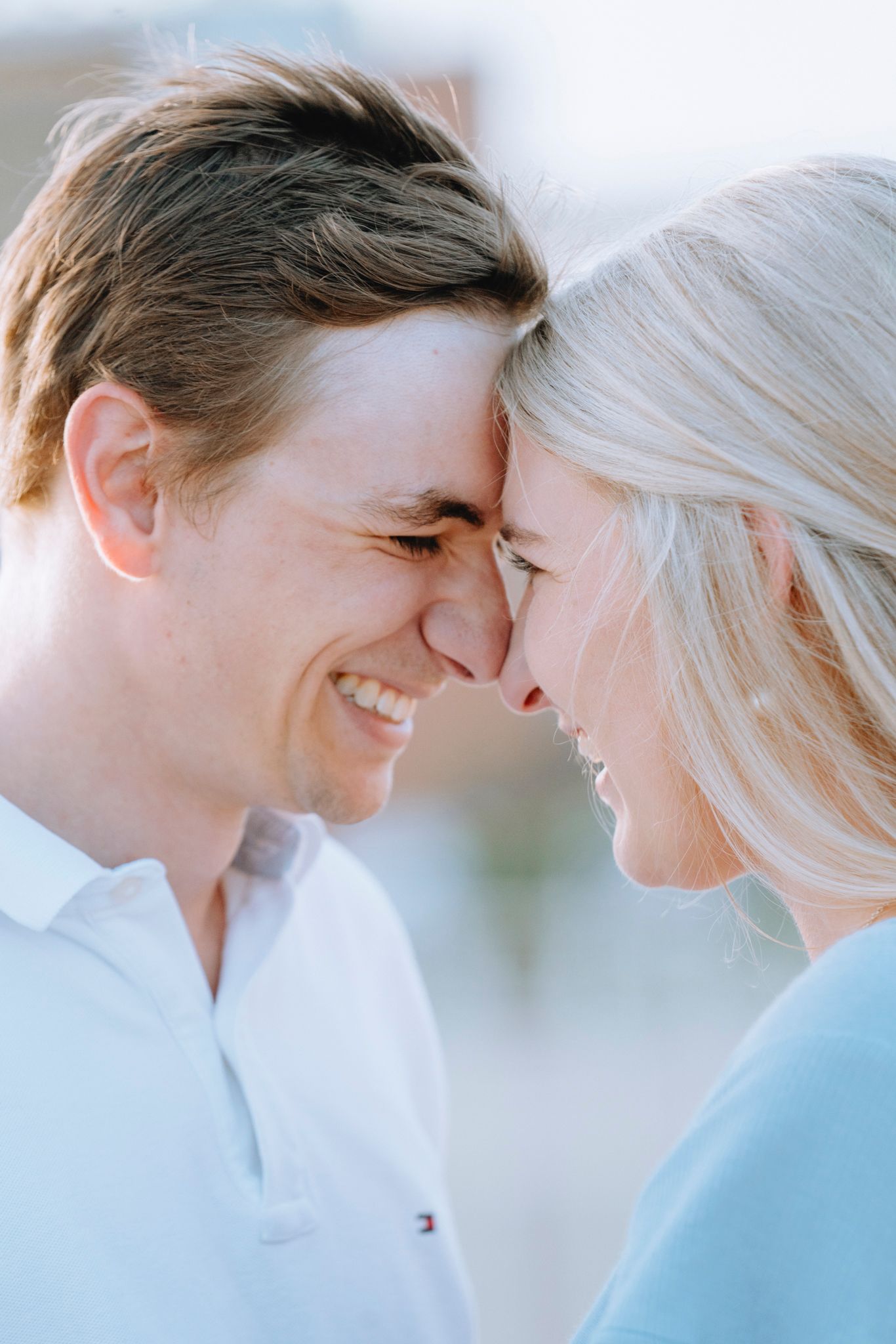 Smiling couple touching foreheads in soft natural light outdoors.
