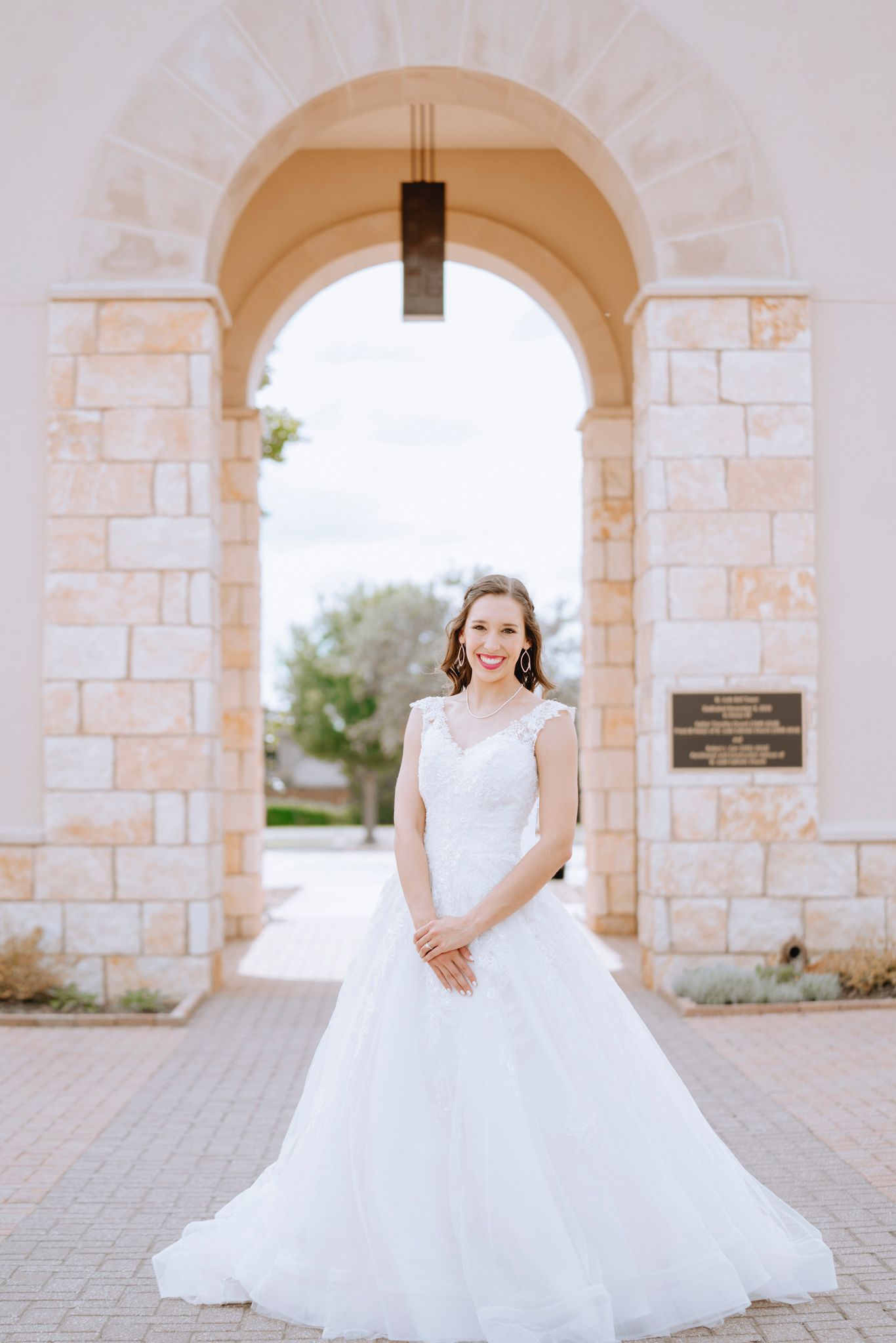 Smiling bride in elegant white ball gown standing under stone arch.