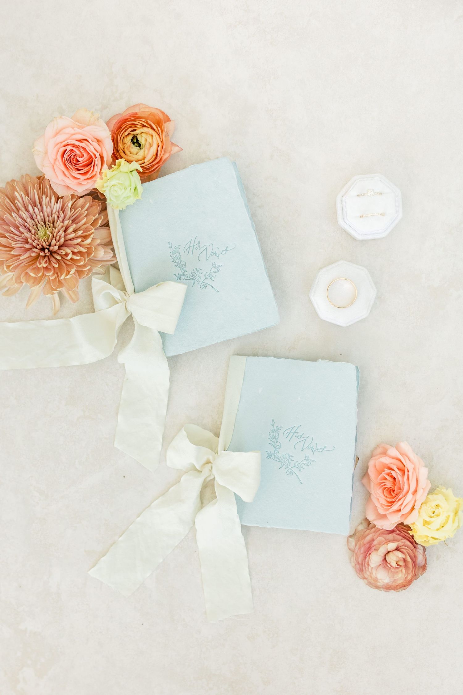 . Two light blue wedding vow books with ribbon bows surrounded by pastel flowers, Wedding rings flatlay photographed on a Tampa wedding day