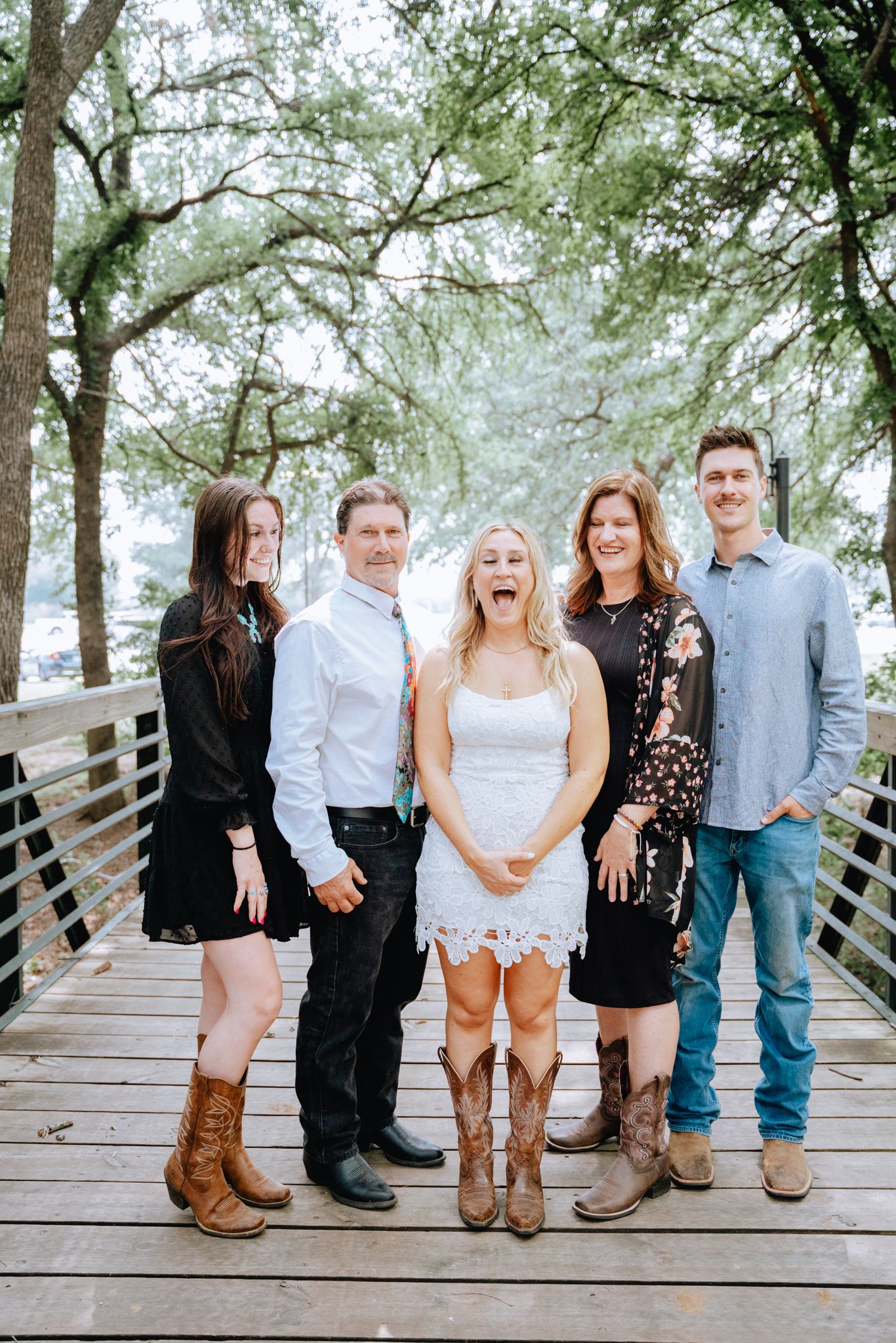Happy family of five posing on a wooden bridge surrounded by trees.