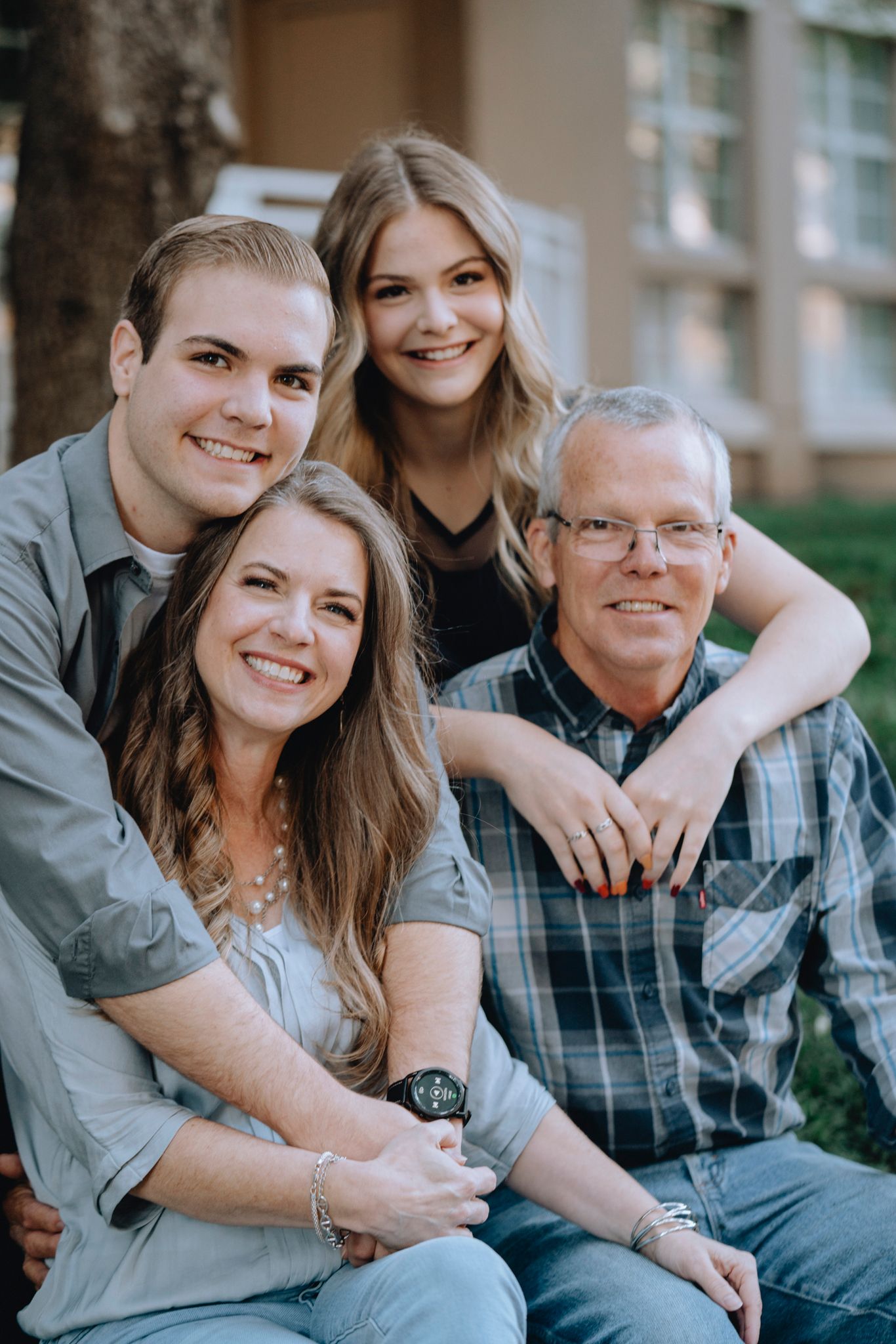 Happy family of four smiling together outdoors near a tree and building.