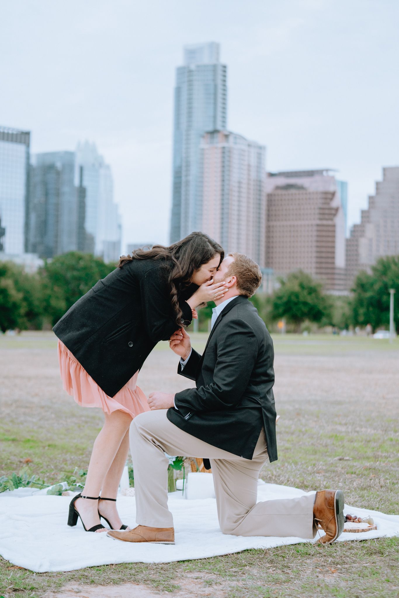 Man proposing on one knee kissing woman in city park.