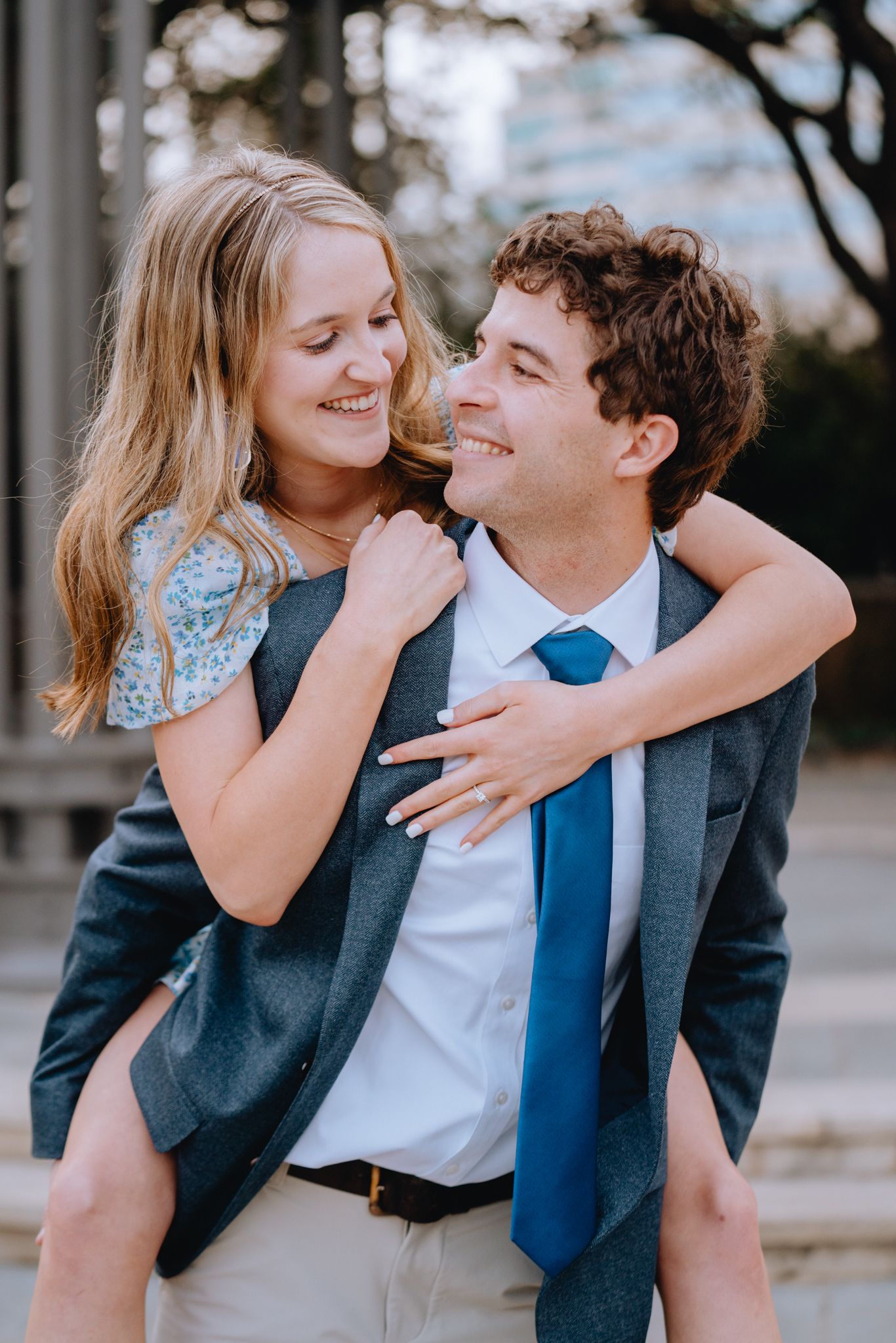 Young woman piggyback riding smiling man in suit outdoors.