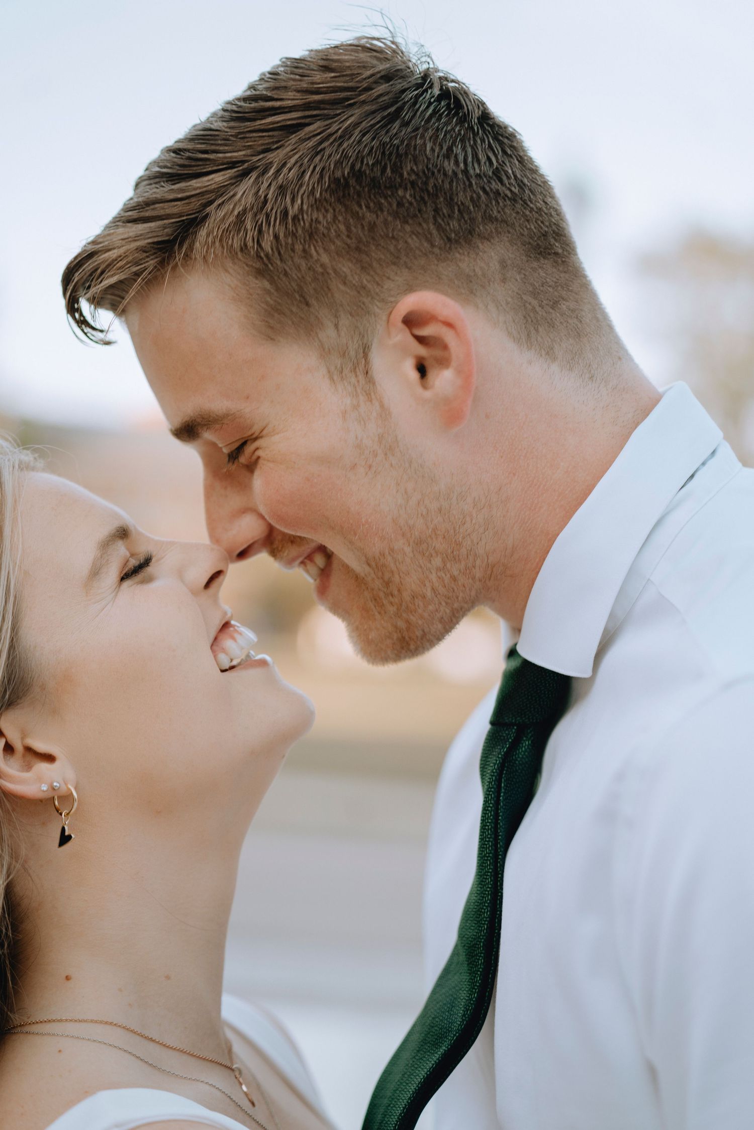 Bride and groom sharing an intimate nose-to-nose moment, groom wearing white shirt and green tie.